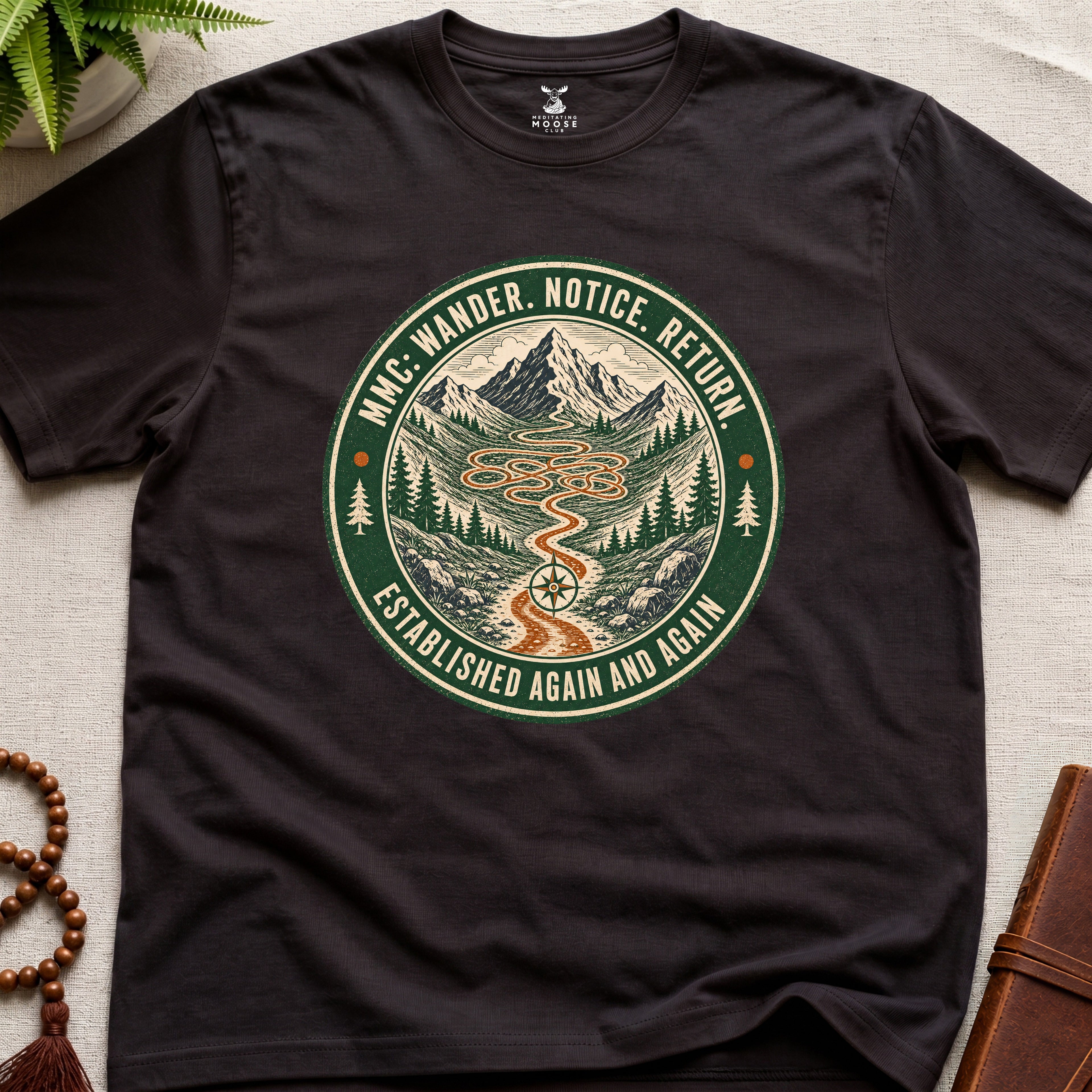 Dark brown mindfulness t-shirt mockup featuring Meditating Moose Club Wander Notice Return mountain trail badge graphic