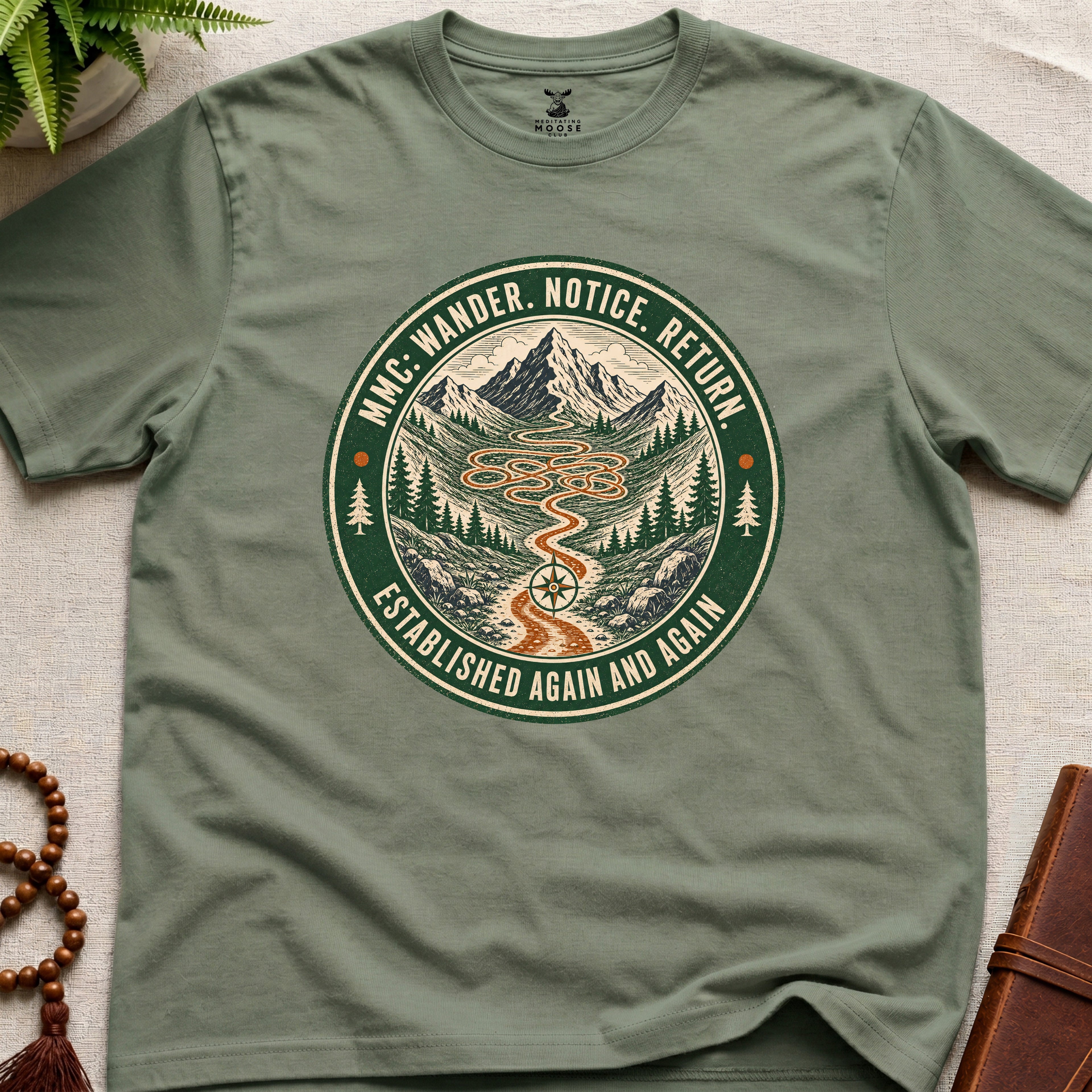 Green mindfulness t-shirt mockup featuring Meditating Moose Club Wander Notice Return mountain trail badge graphic