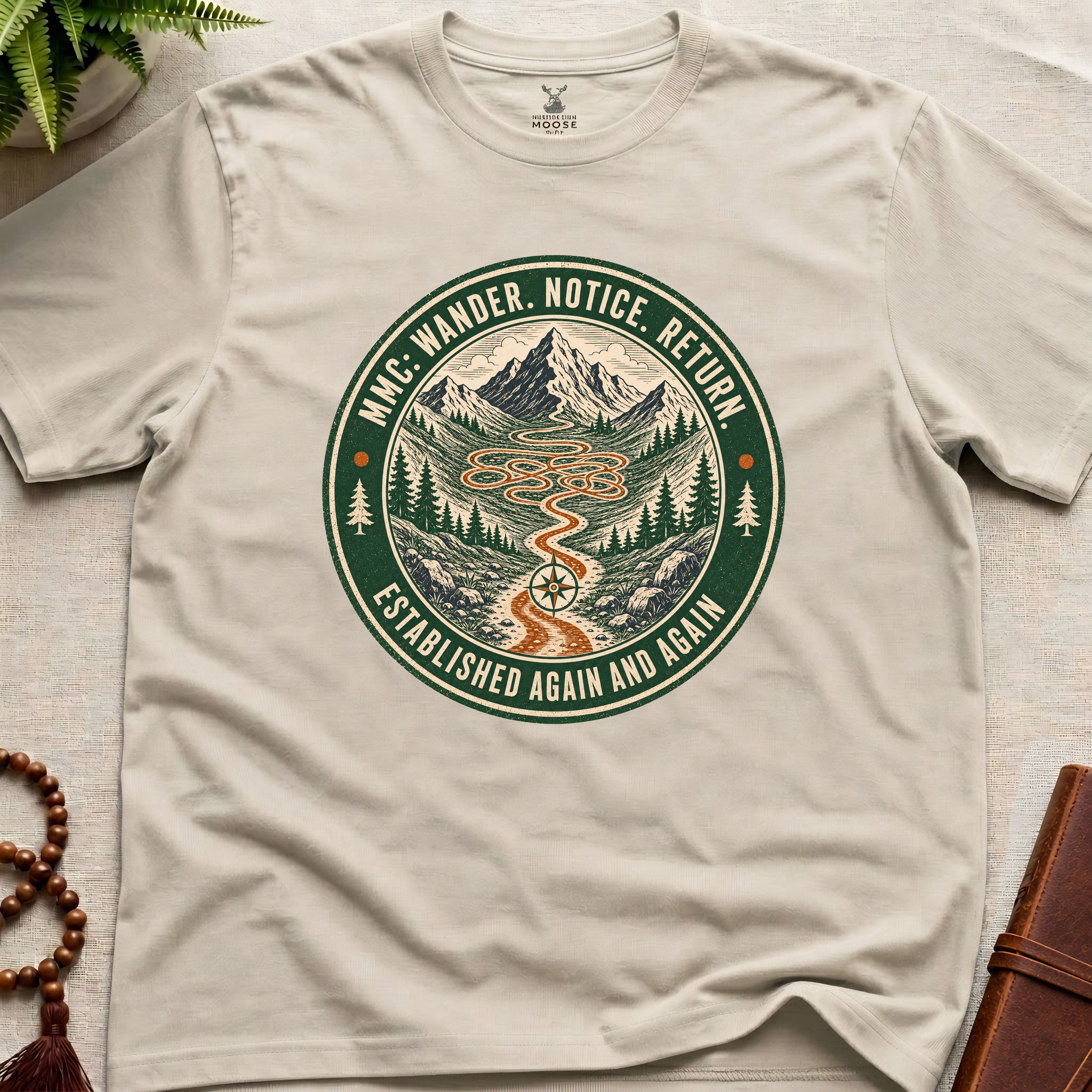 Beige mindfulness t-shirt mockup featuring Meditating Moose Club Wander Notice Return mountain trail badge graphic