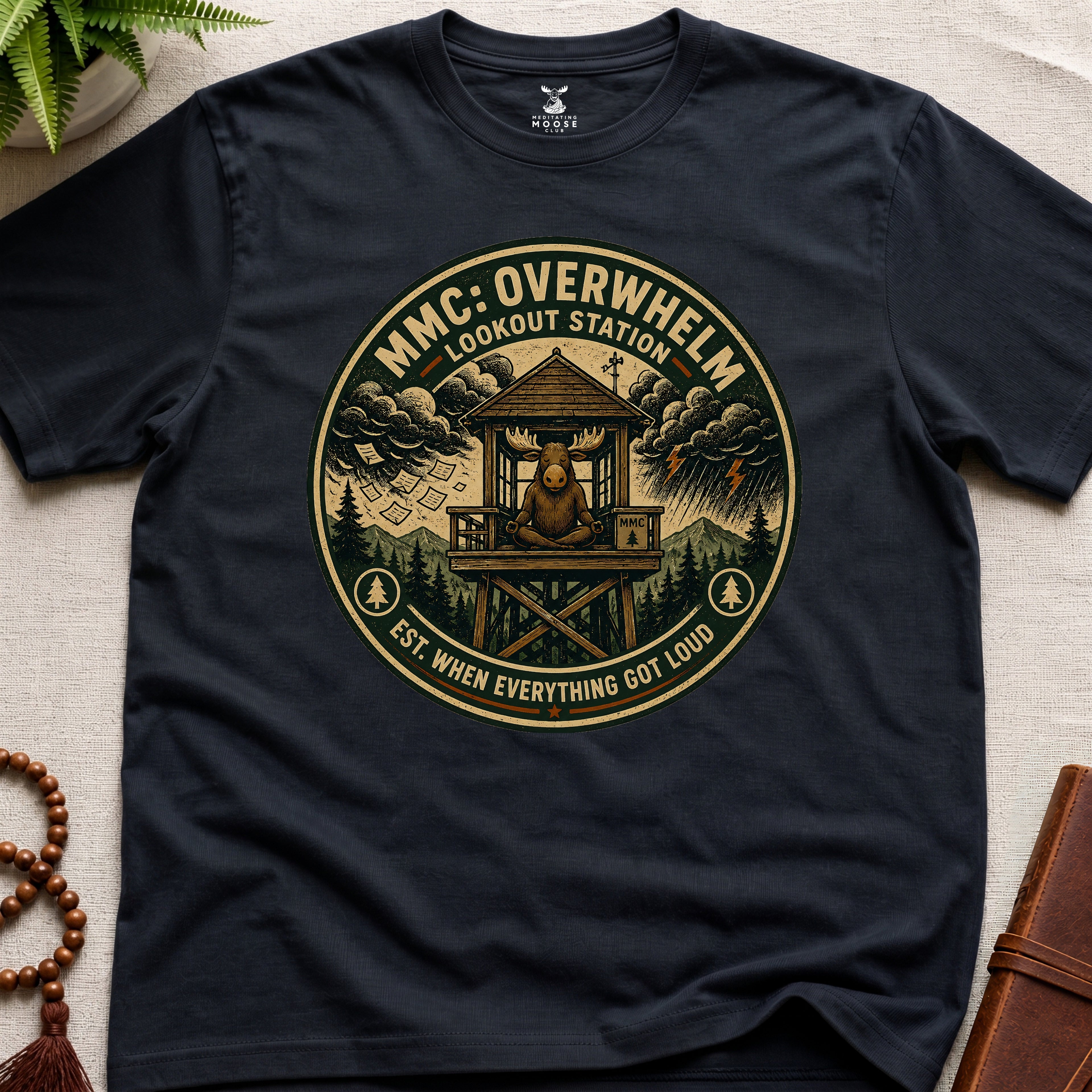Black mindfulness t-shirt mockup featuring Overwhelm Lookout Station meditating moose stress graphic