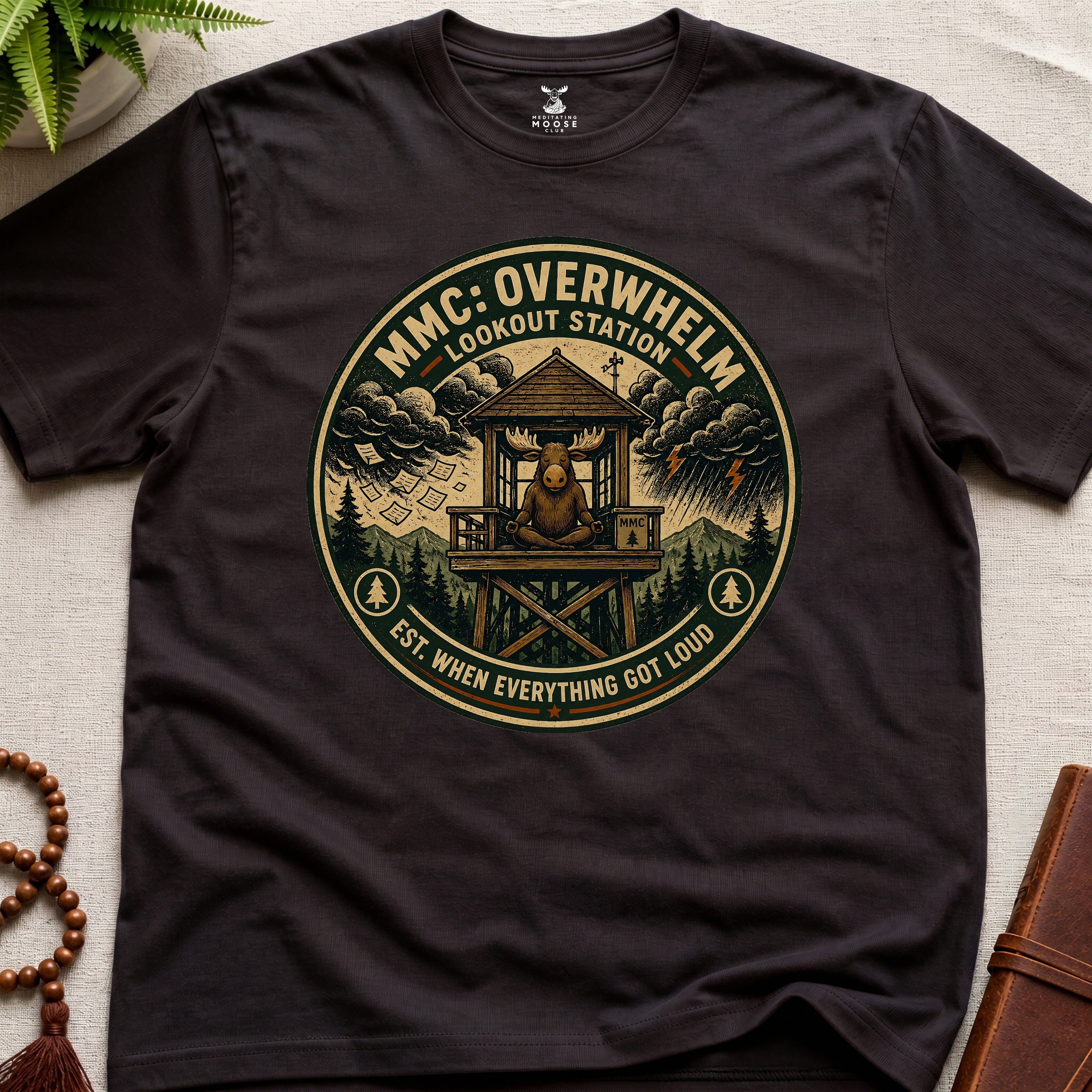 Dark brown mindfulness t-shirt mockup featuring Overwhelm Lookout Station meditating moose stress graphic