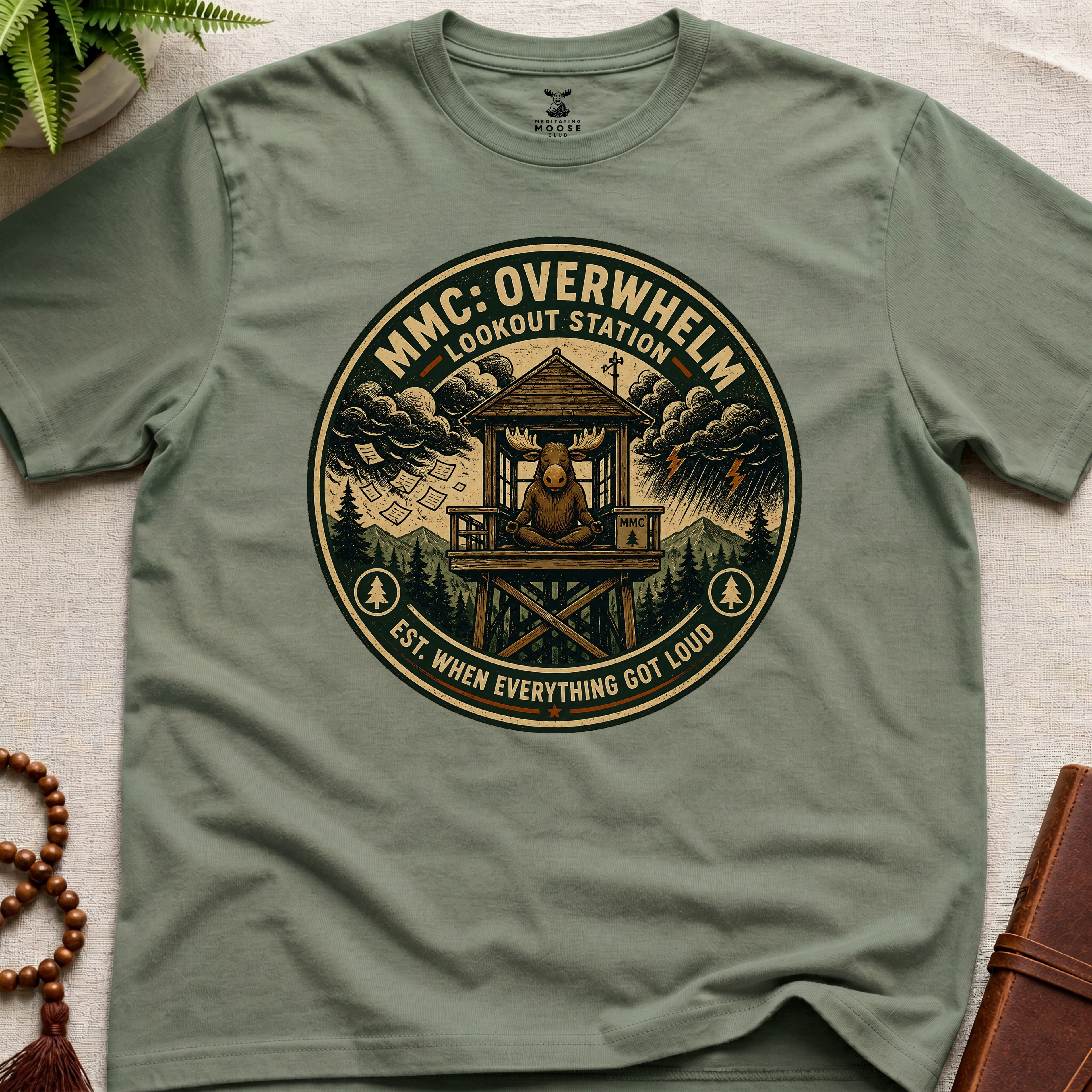 Green mindfulness t-shirt mockup featuring Overwhelm Lookout Station meditating moose stress graphic