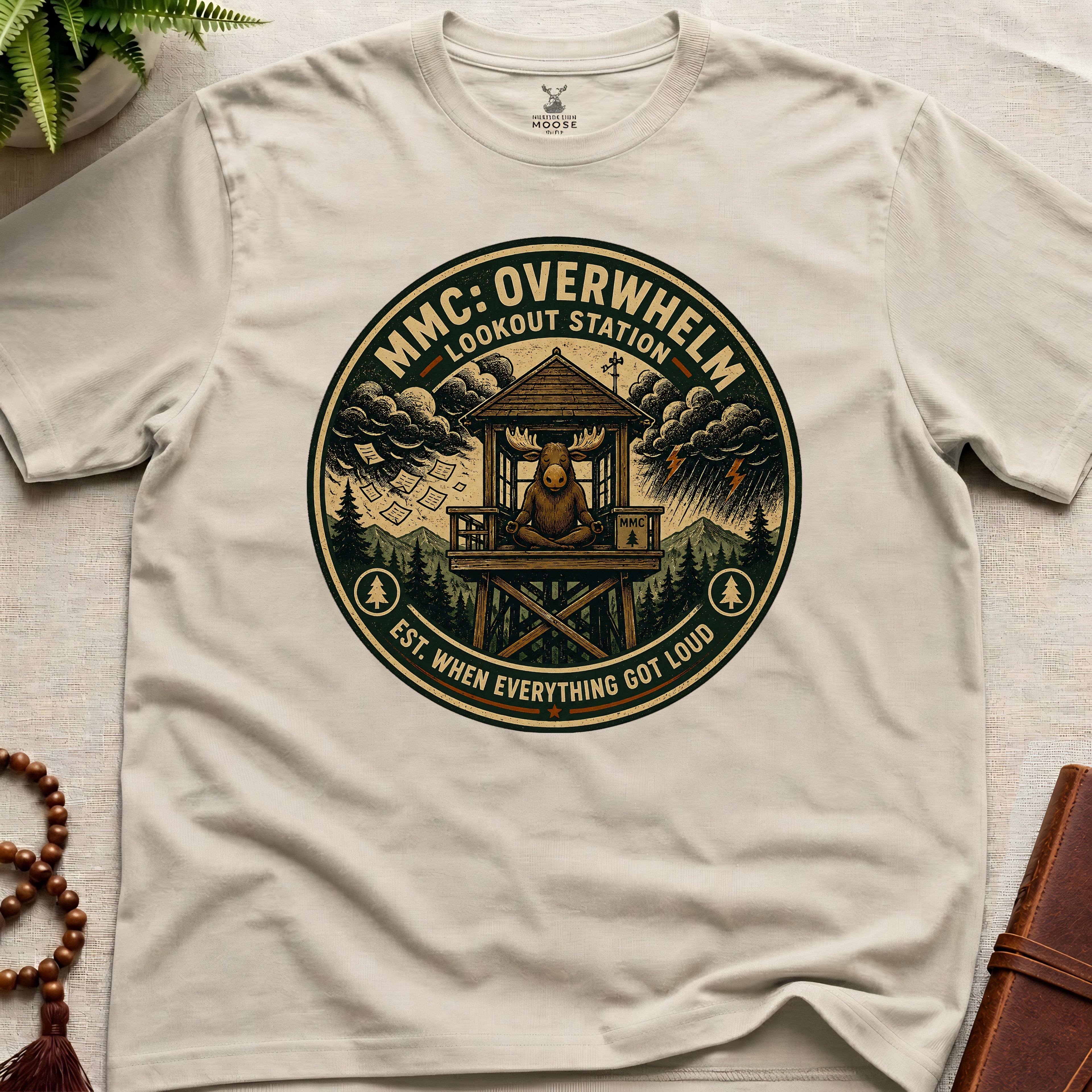Beige mindfulness t-shirt mockup featuring Overwhelm Lookout Station meditating moose stress graphic