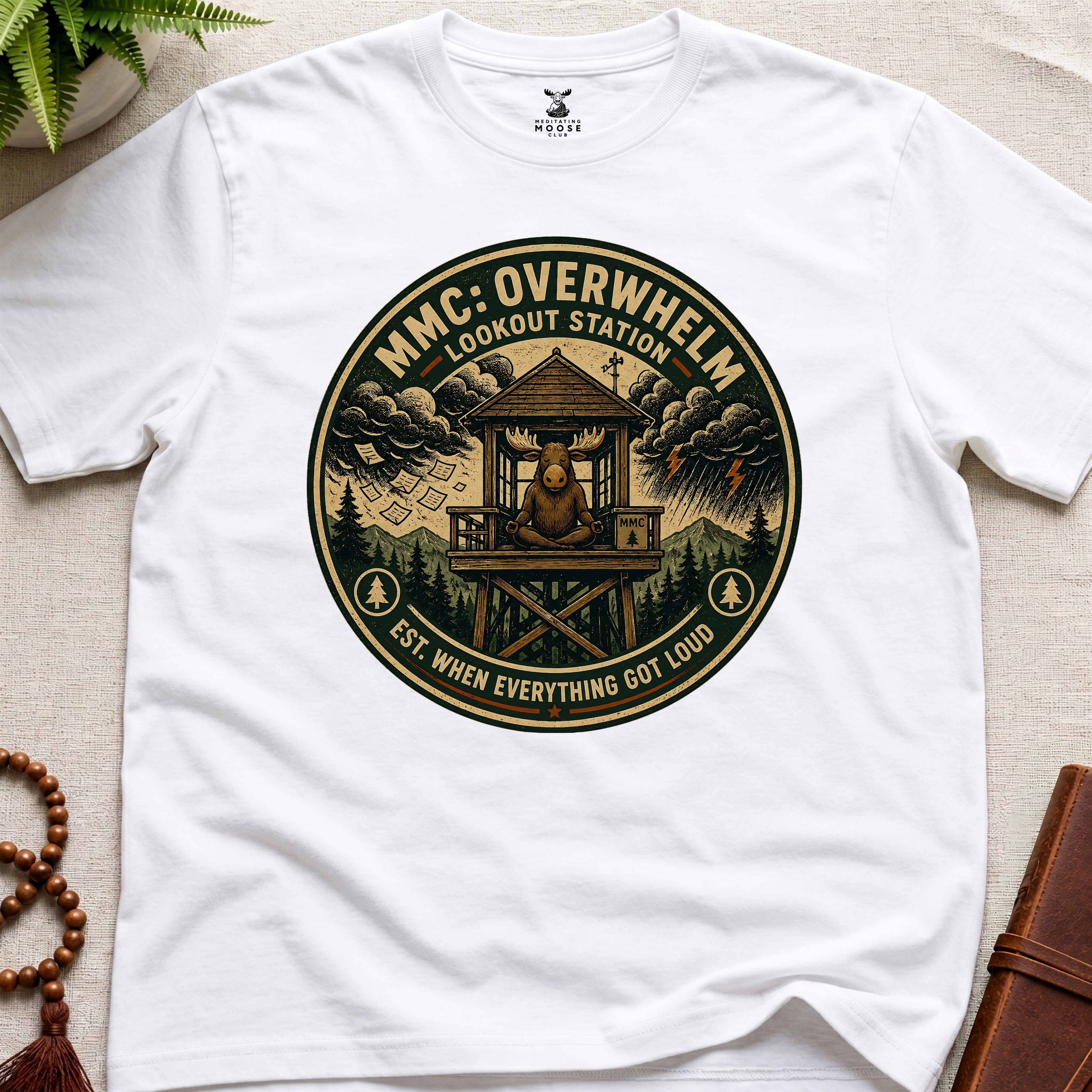 White mindfulness t-shirt mockup featuring Overwhelm Lookout Station meditating moose stress graphic
