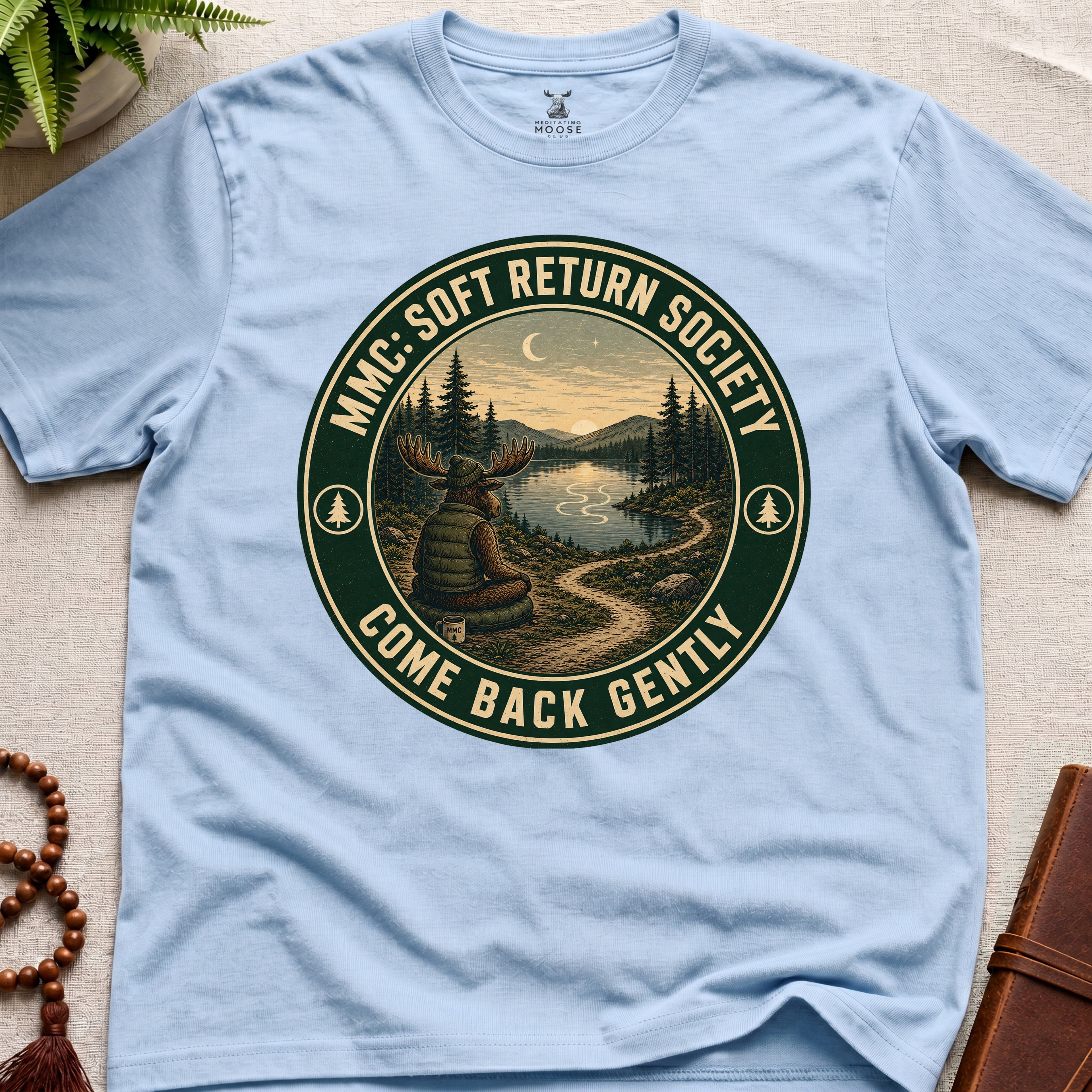 Light blue mindfulness t-shirt mockup featuring Soft Return Society vintage wilderness meditation badge design