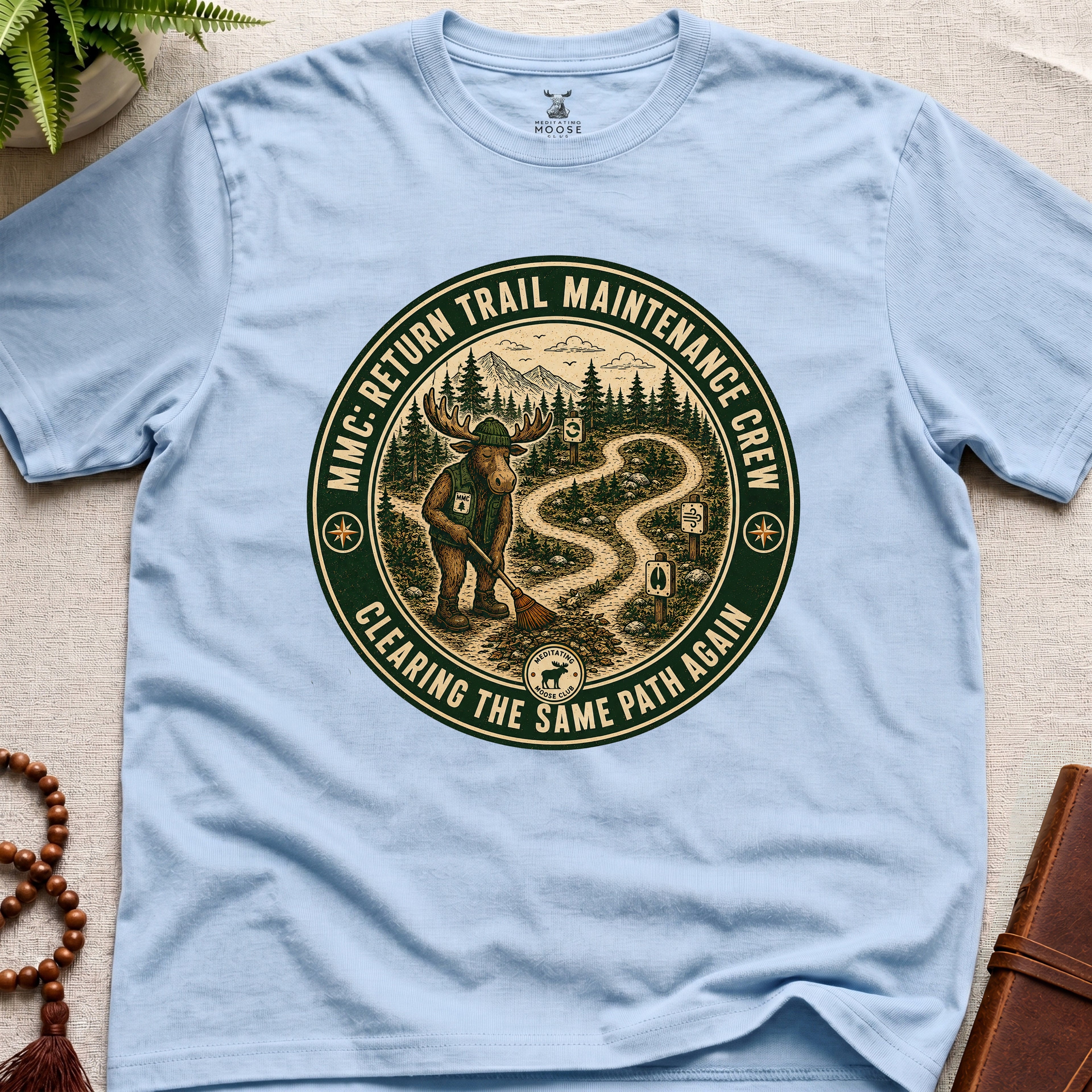 Light blue mindfulness t-shirt mockup featuring Return Trail Maintenance Crew meditating moose vintage badge graphic
