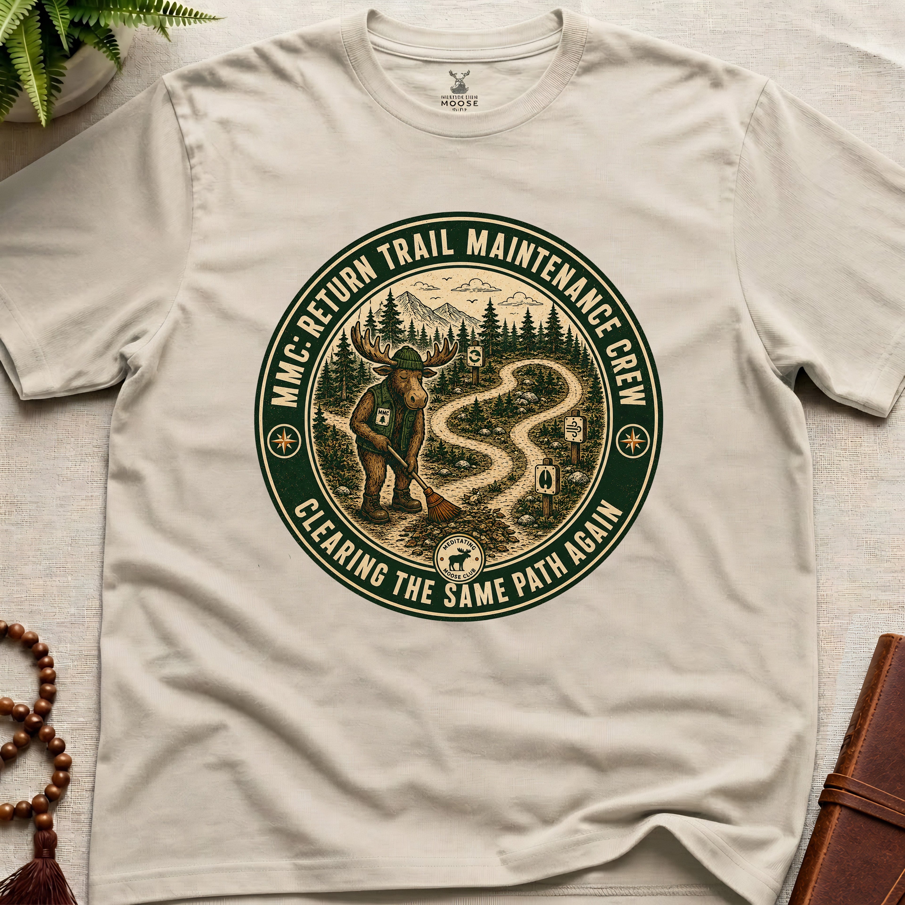 Beige mindfulness t-shirt mockup featuring Return Trail Maintenance Crew meditating moose vintage badge graphic