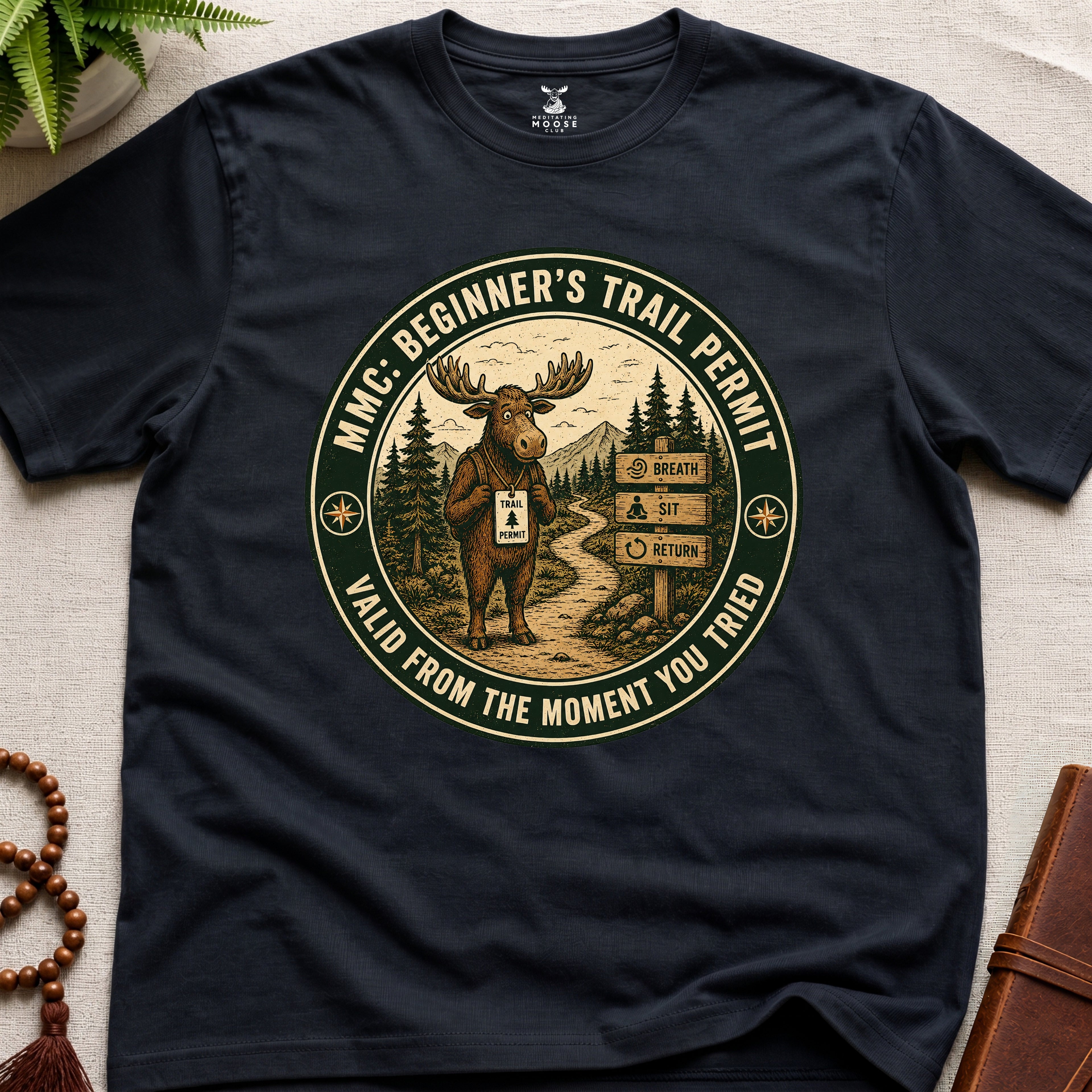 Black mindfulness t-shirt mockup featuring Beginner’s Trail Permit meditating moose beginner meditation graphic