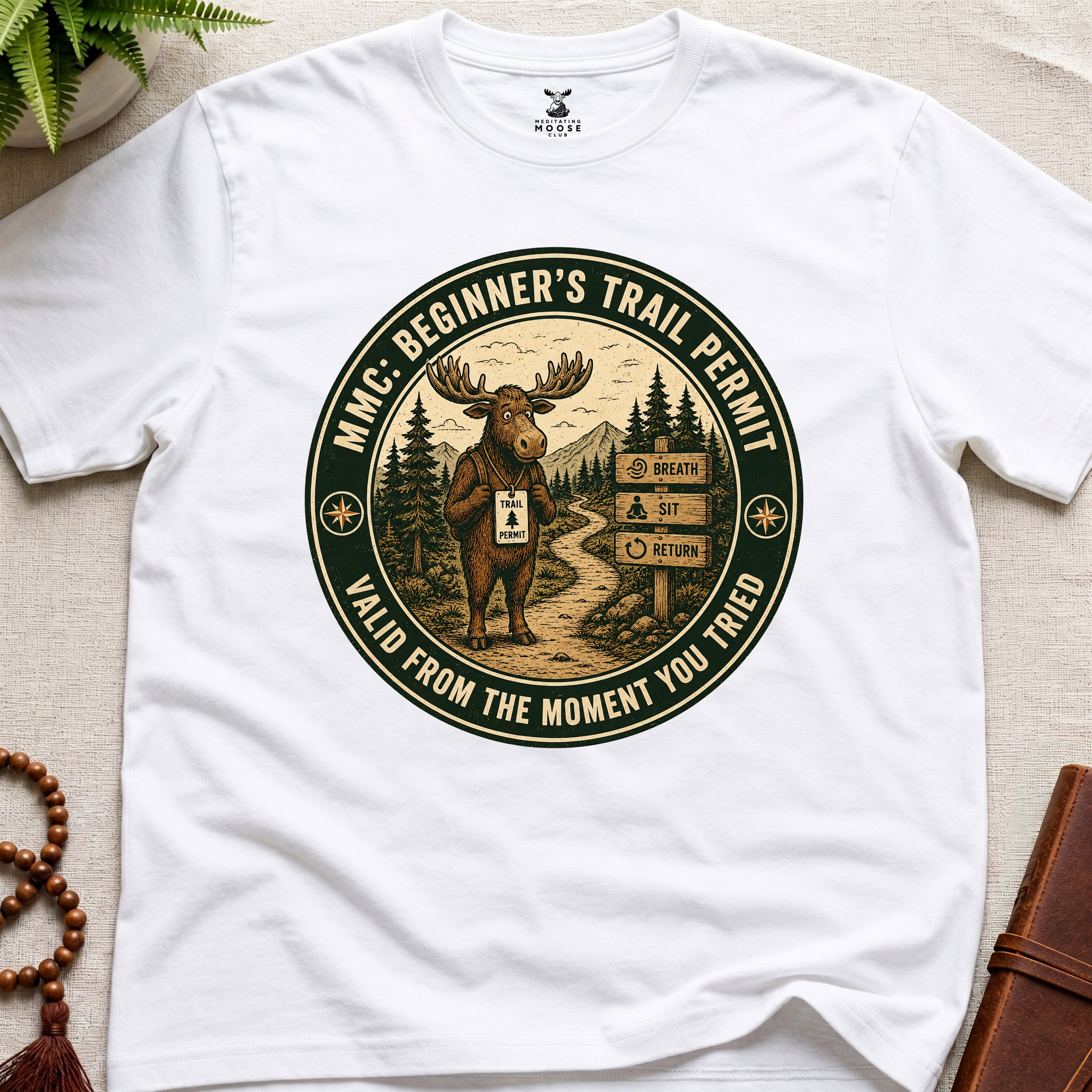 White mindfulness t-shirt mockup featuring Beginner’s Trail Permit meditating moose beginner meditation graphic