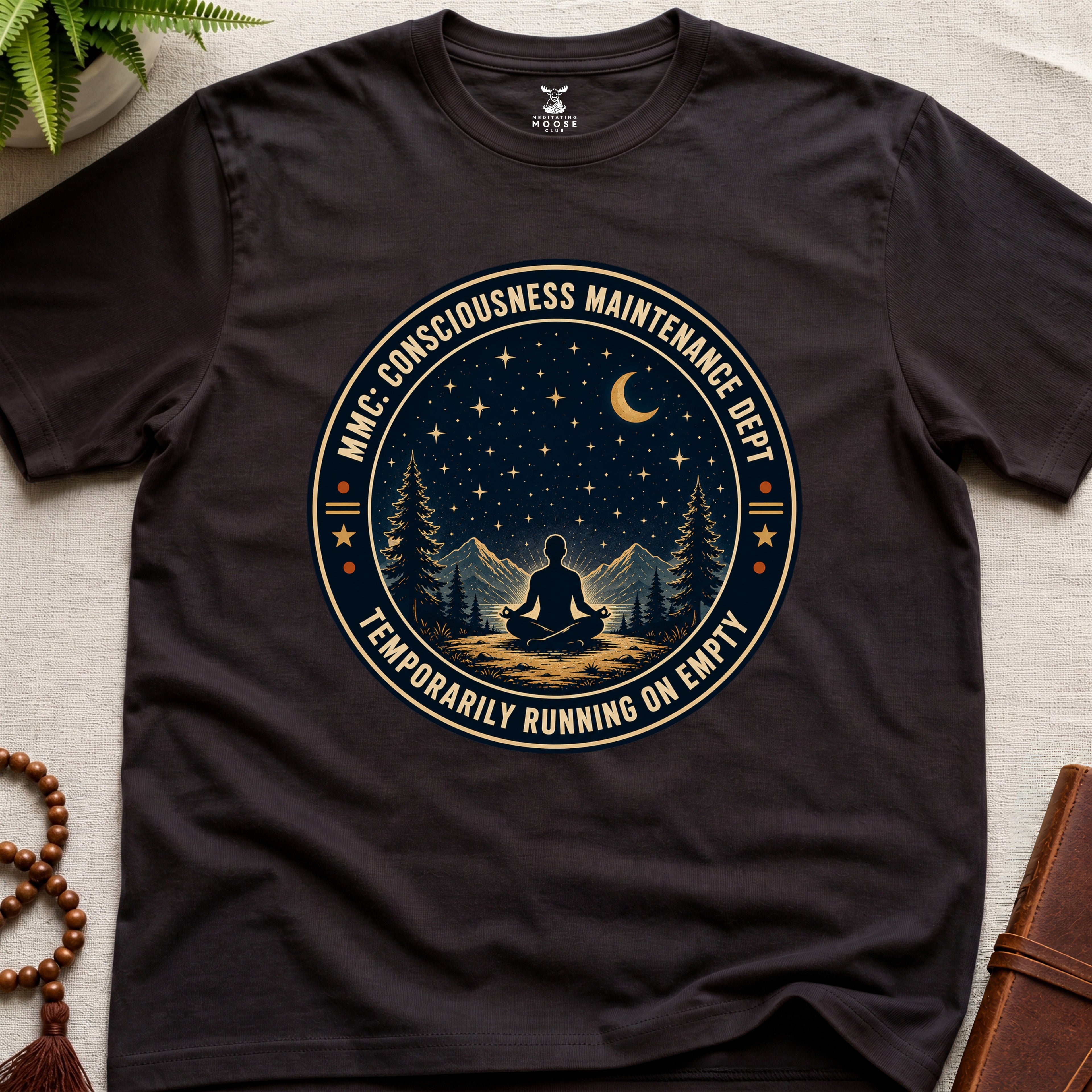 Dark brown mindfulness t-shirt with a circular badge design featuring a meditating figure and trees - consciousness maintenance dept.