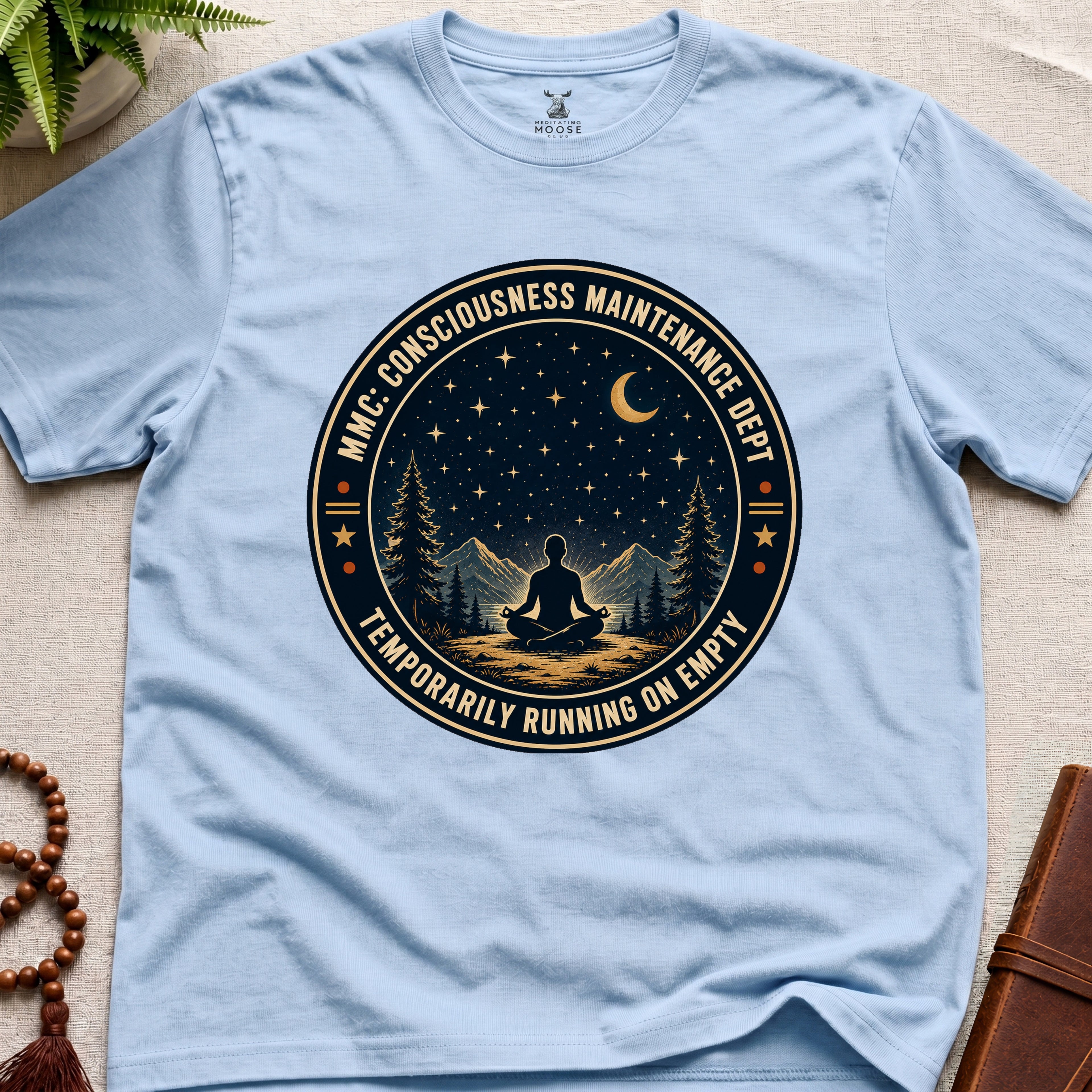 Light blue mindfulness t-shirt with a circular badge design featuring a meditating figure and trees - consciousness maintenance dept.