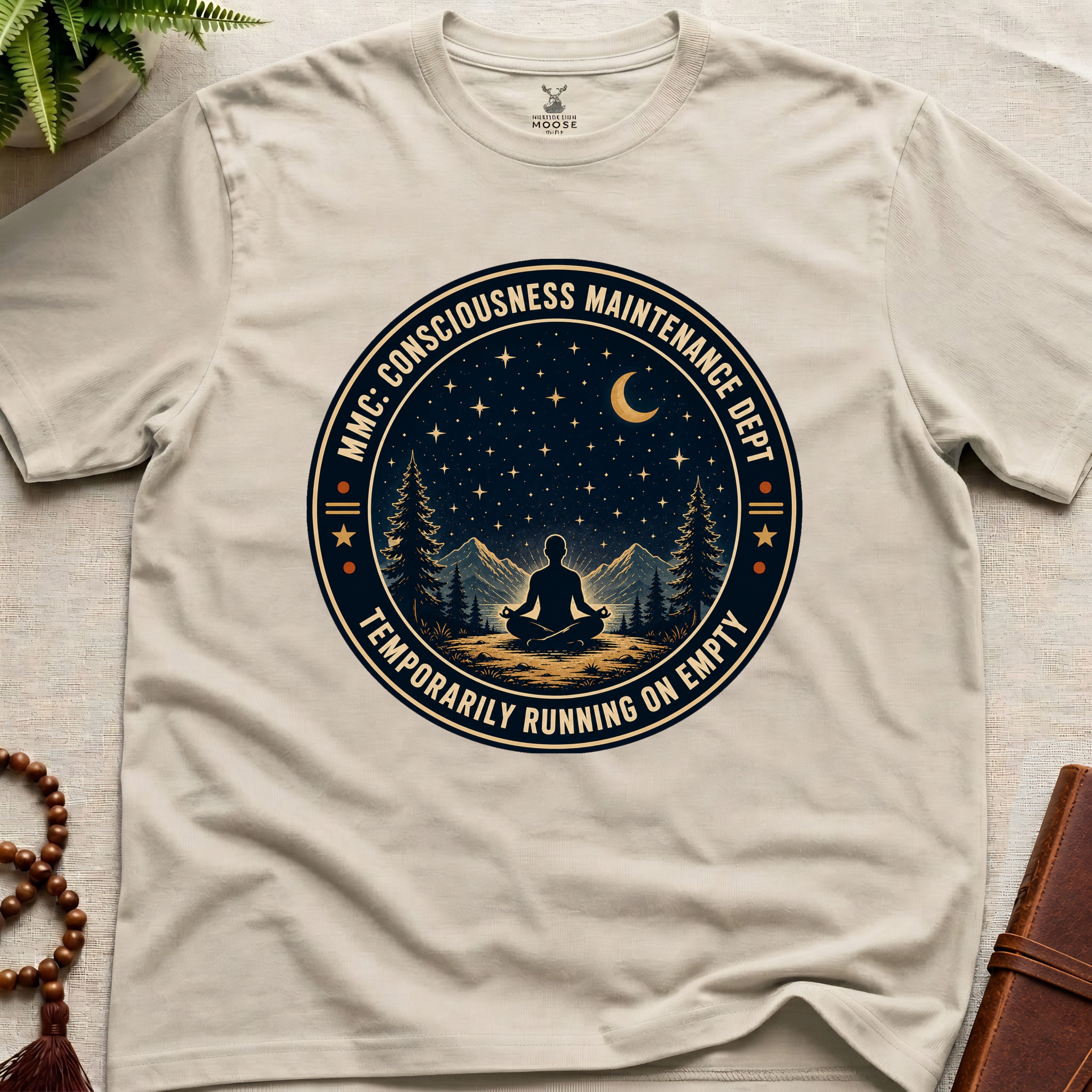 Beige mindfulness t-shirt with a circular badge design featuring a meditating figure and trees - consciousness maintenance dept.