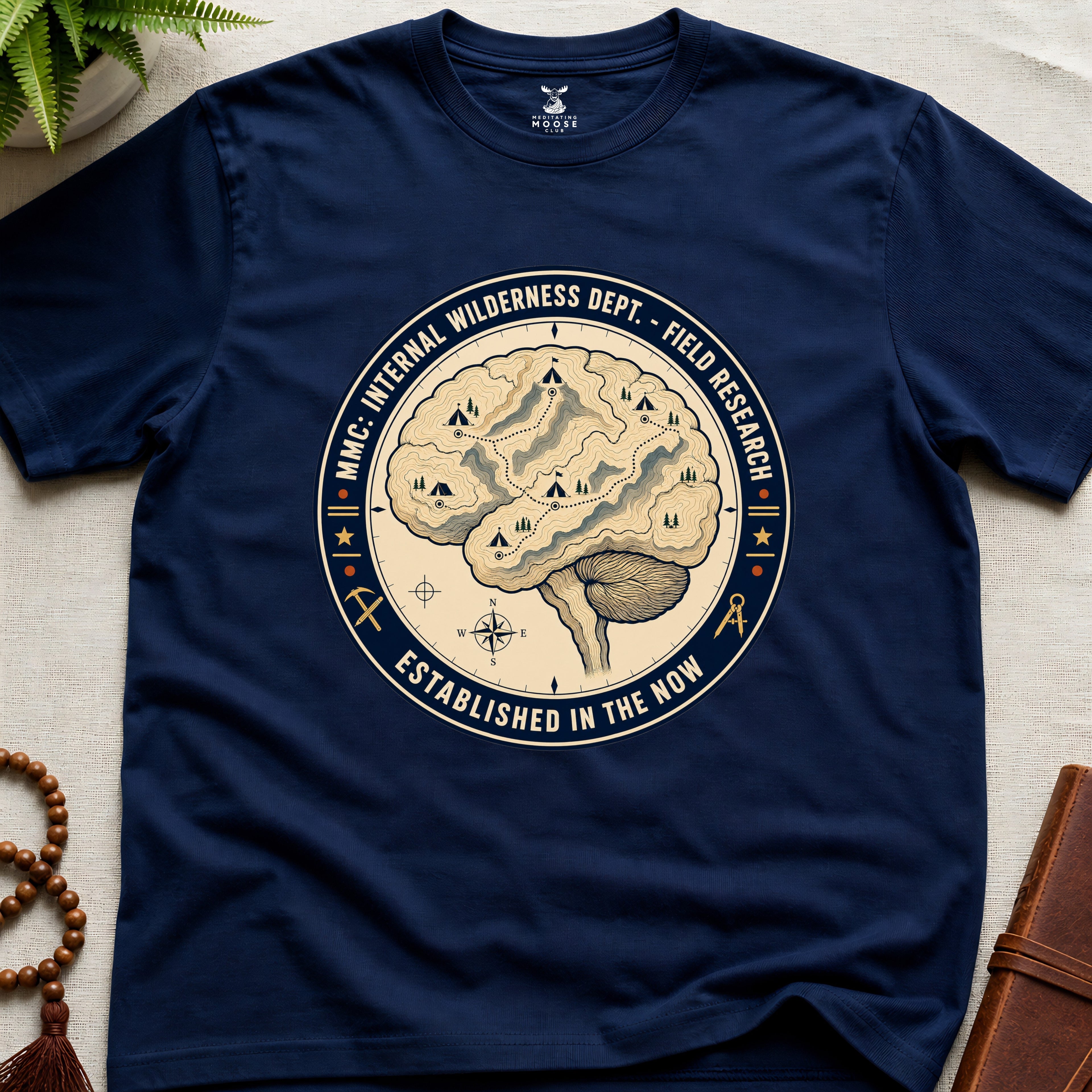 Navy blue t-shirt with a circular graphic design featuring a brain and wilderness elements on a beige surface.