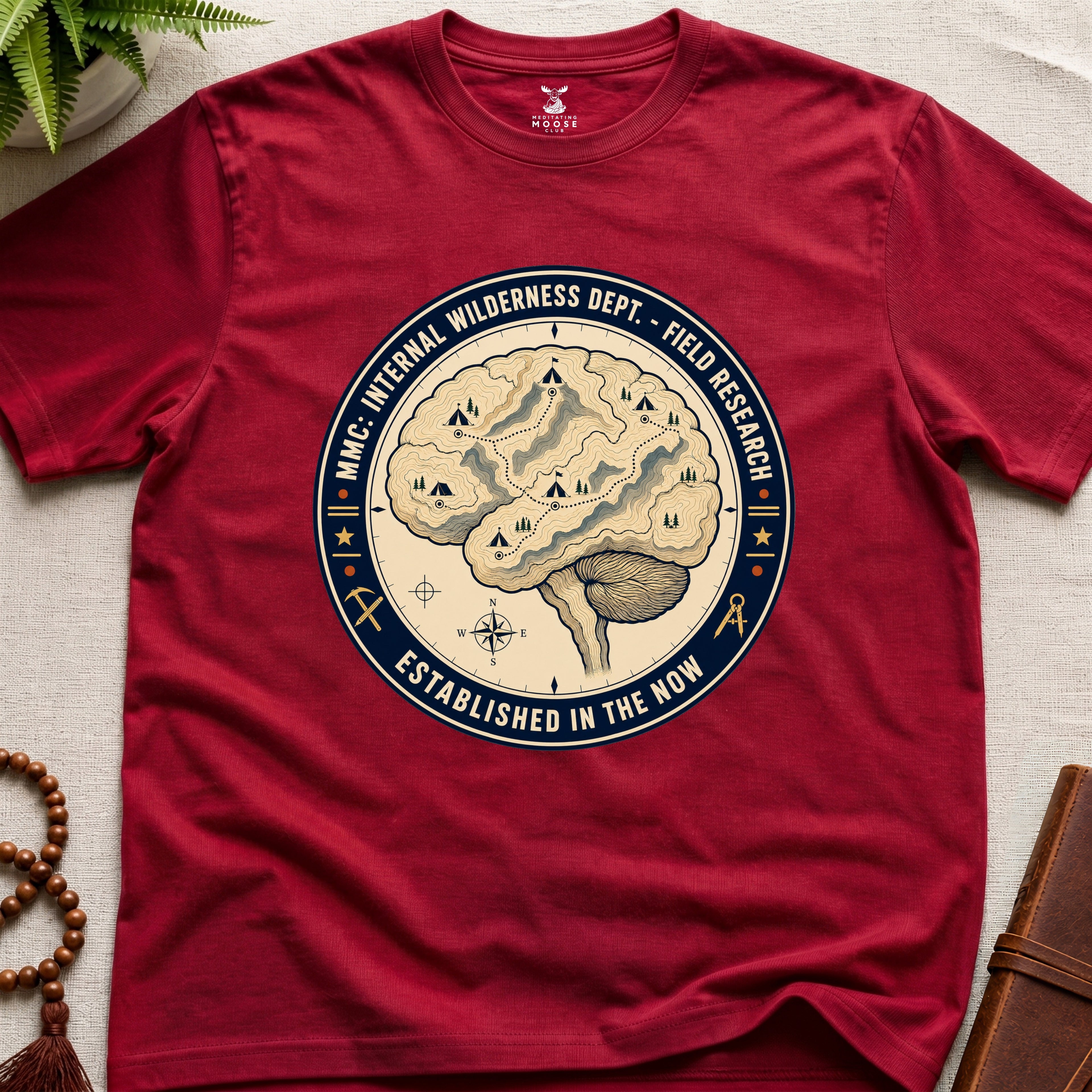 Red t-shirt with a circular graphic design featuring a brain and wilderness elements on a beige surface.
