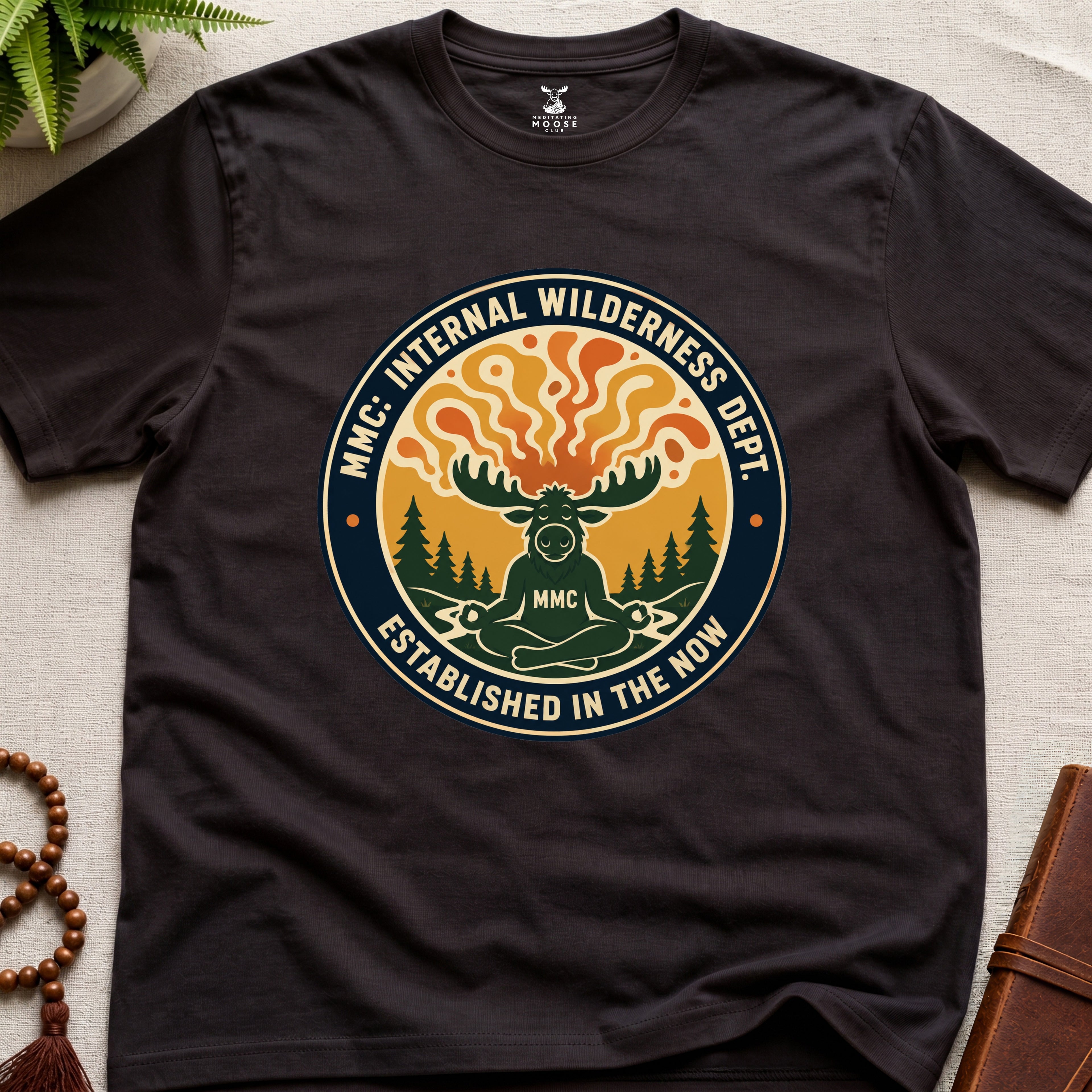 Dark brown t-shirt with a circular graphic design featuring a moose and trees on a beige surface.