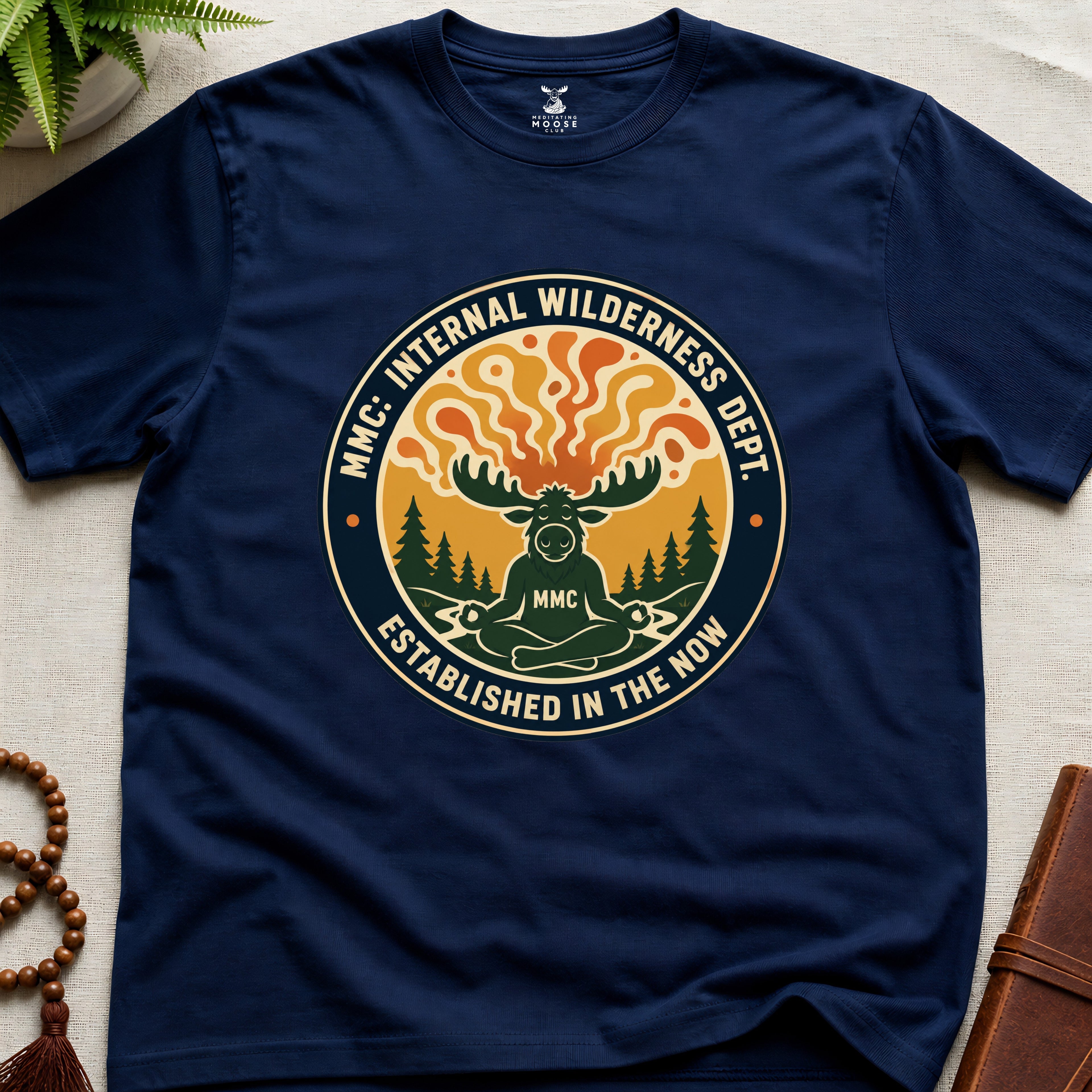 Navy blue t-shirt with a circular graphic design featuring a moose and trees on a beige surface.