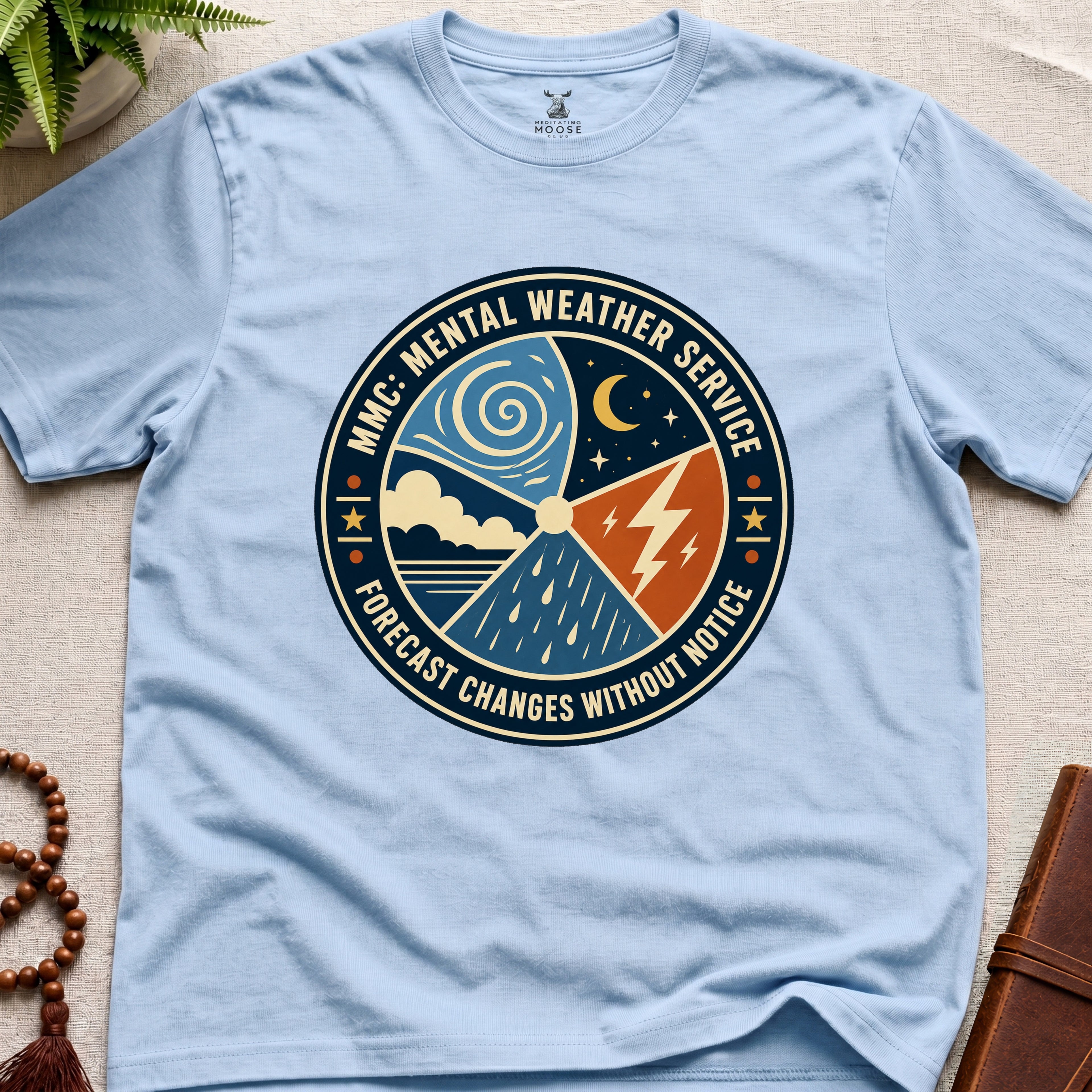 Light blue t-shirt with a circular graphic design mental weather service on a light surface.