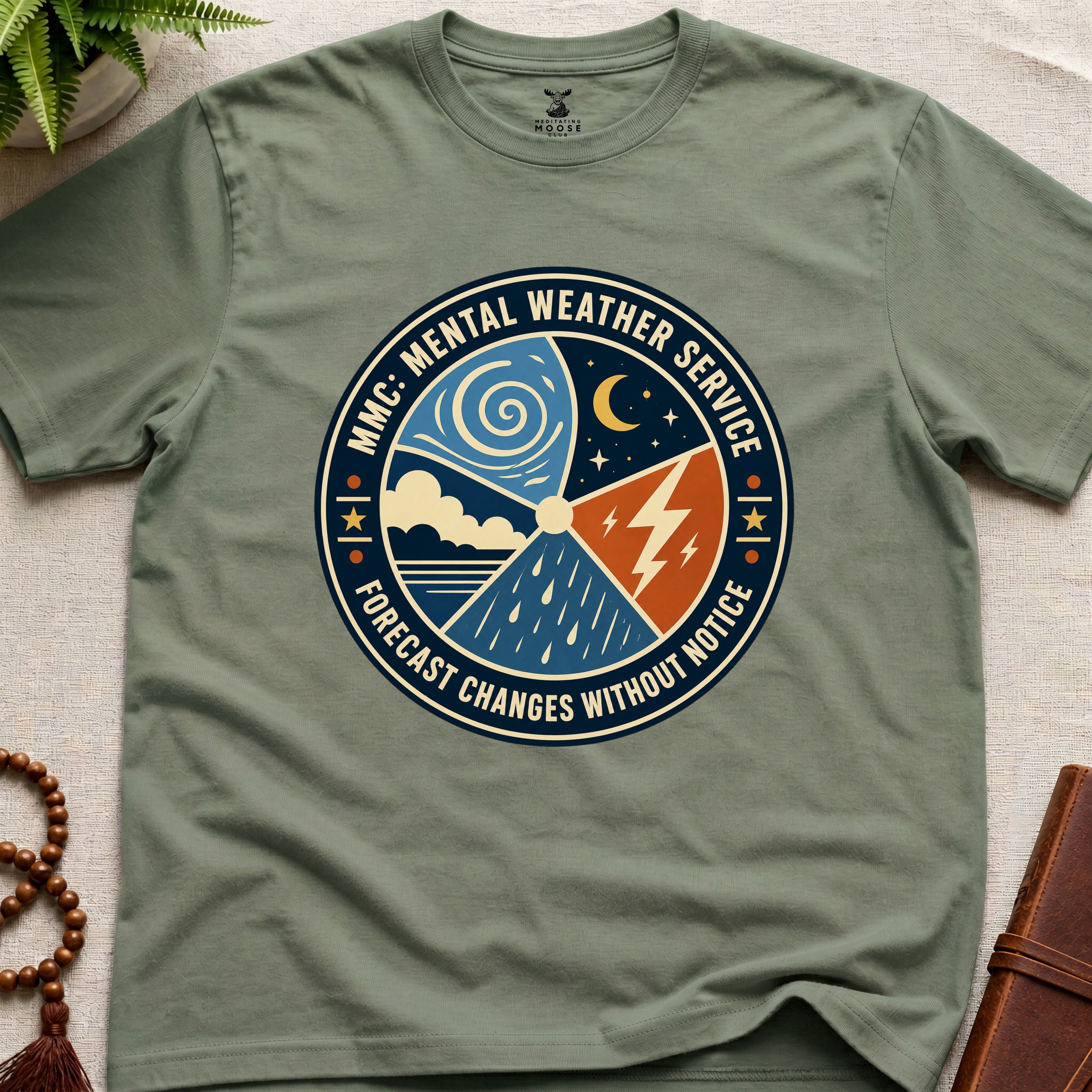 Military green t-shirt with a circular graphic design mental weather service on a light surface.