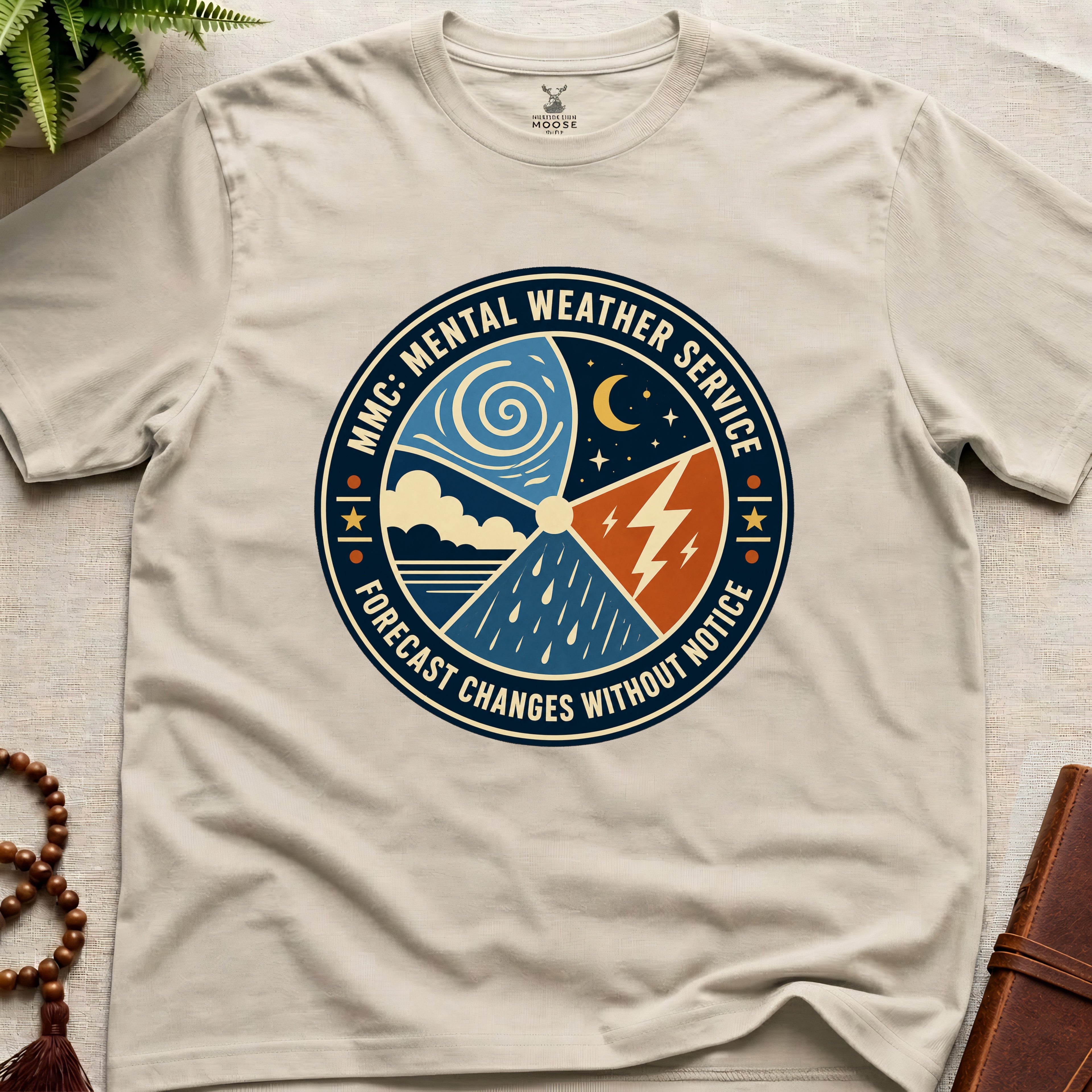 Beige t-shirt with a circular graphic design mental weather service on a light surface.