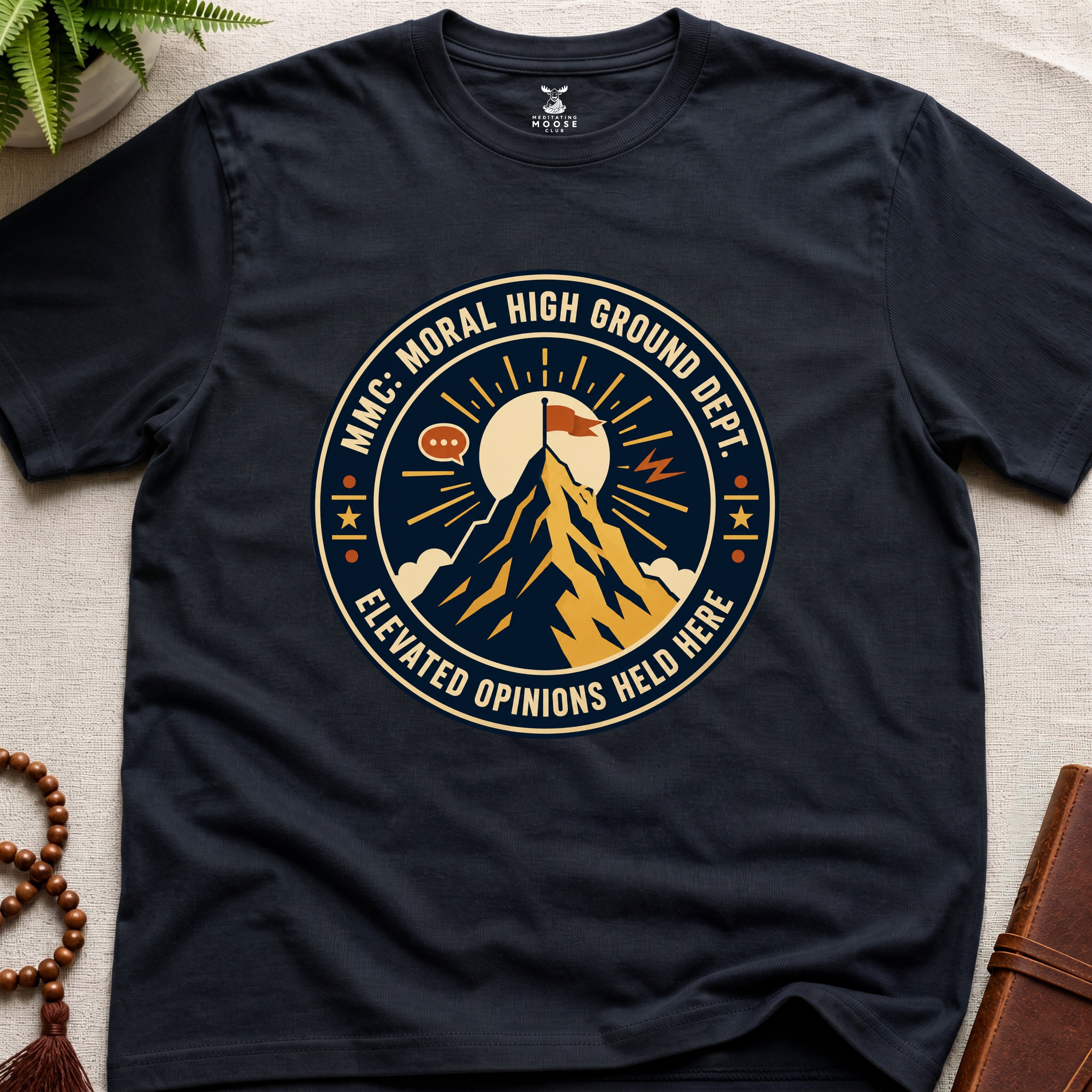 Black t-shirt badge graphic with a mountain and text "moral High Ground Dept." on a light surface.
