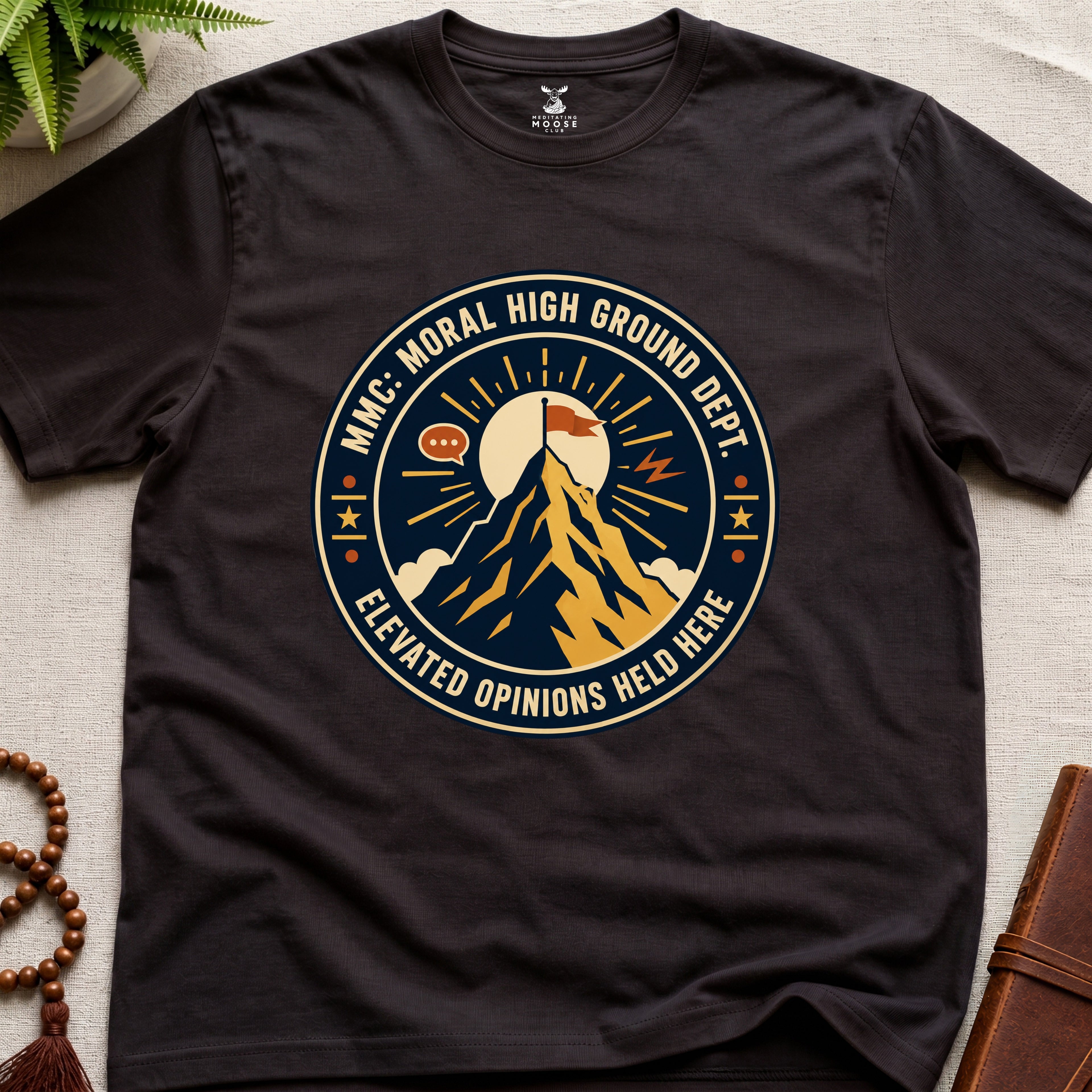 Dark brown t-shirt badge graphic with a mountain and text "moral High Ground Dept." on a light surface.