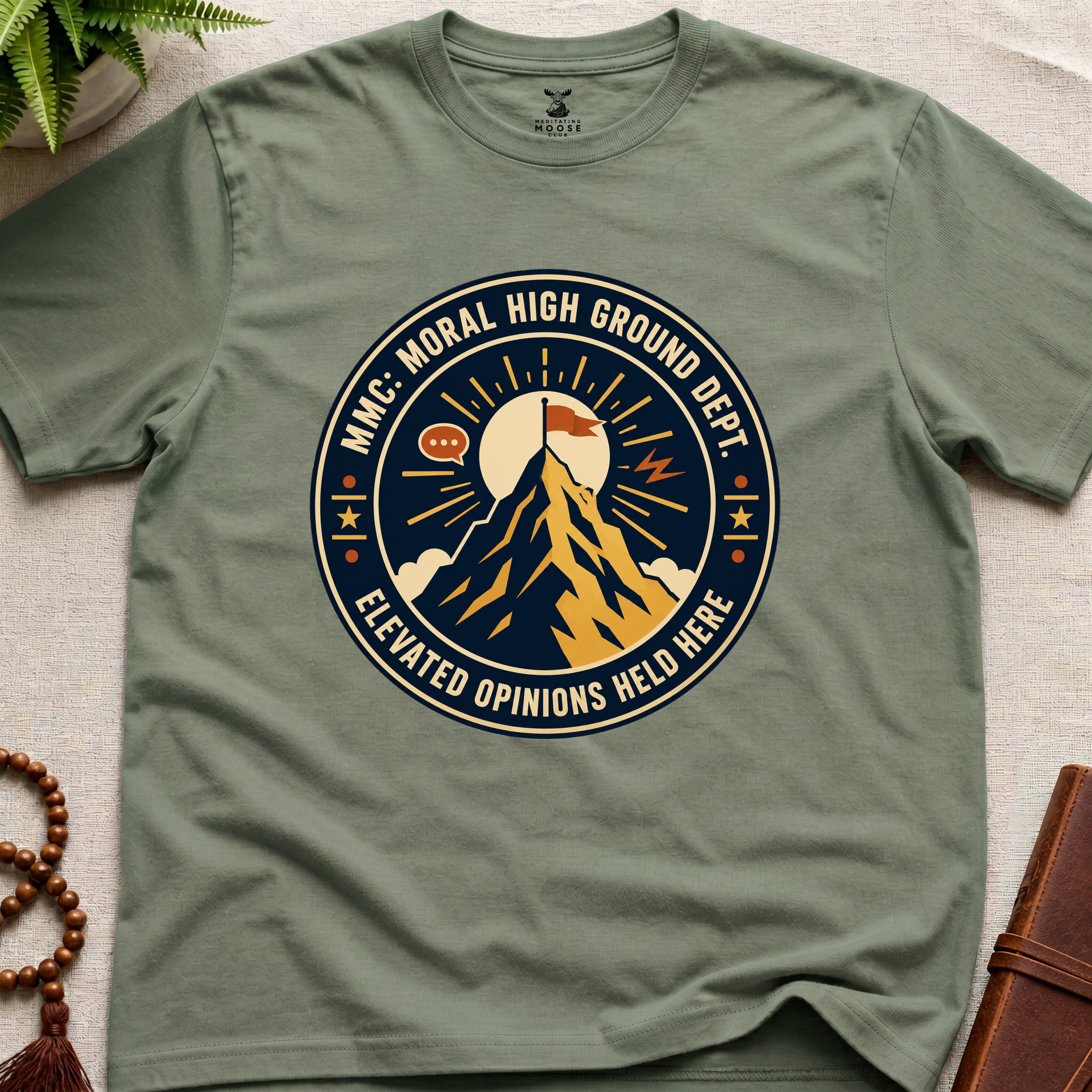 Military green t-shirt badge graphic with a mountain and text "moral High Ground Dept." on a light surface.