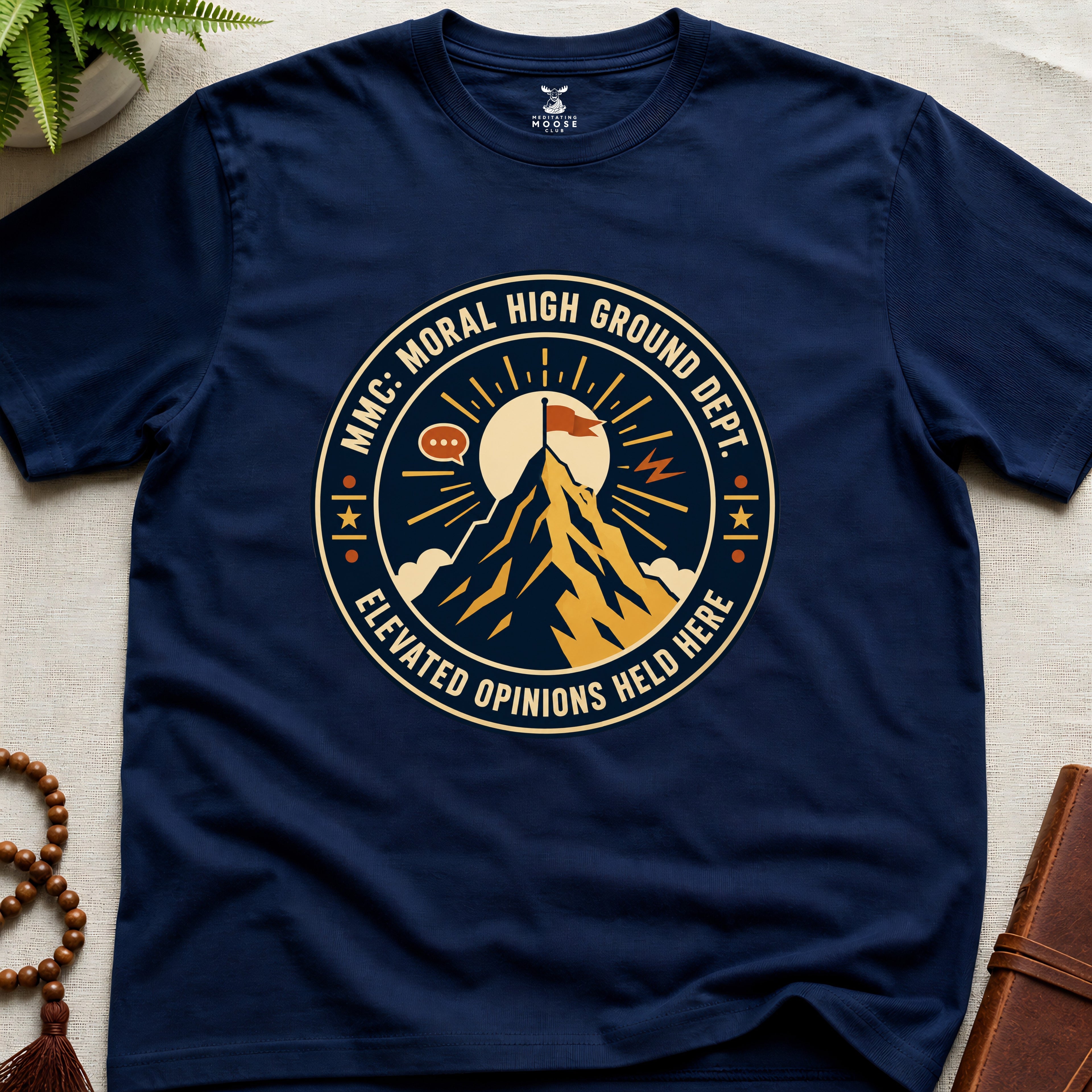 Navy blue t-shirt badge graphic with a mountain and text "moral High Ground Dept." on a light surface.