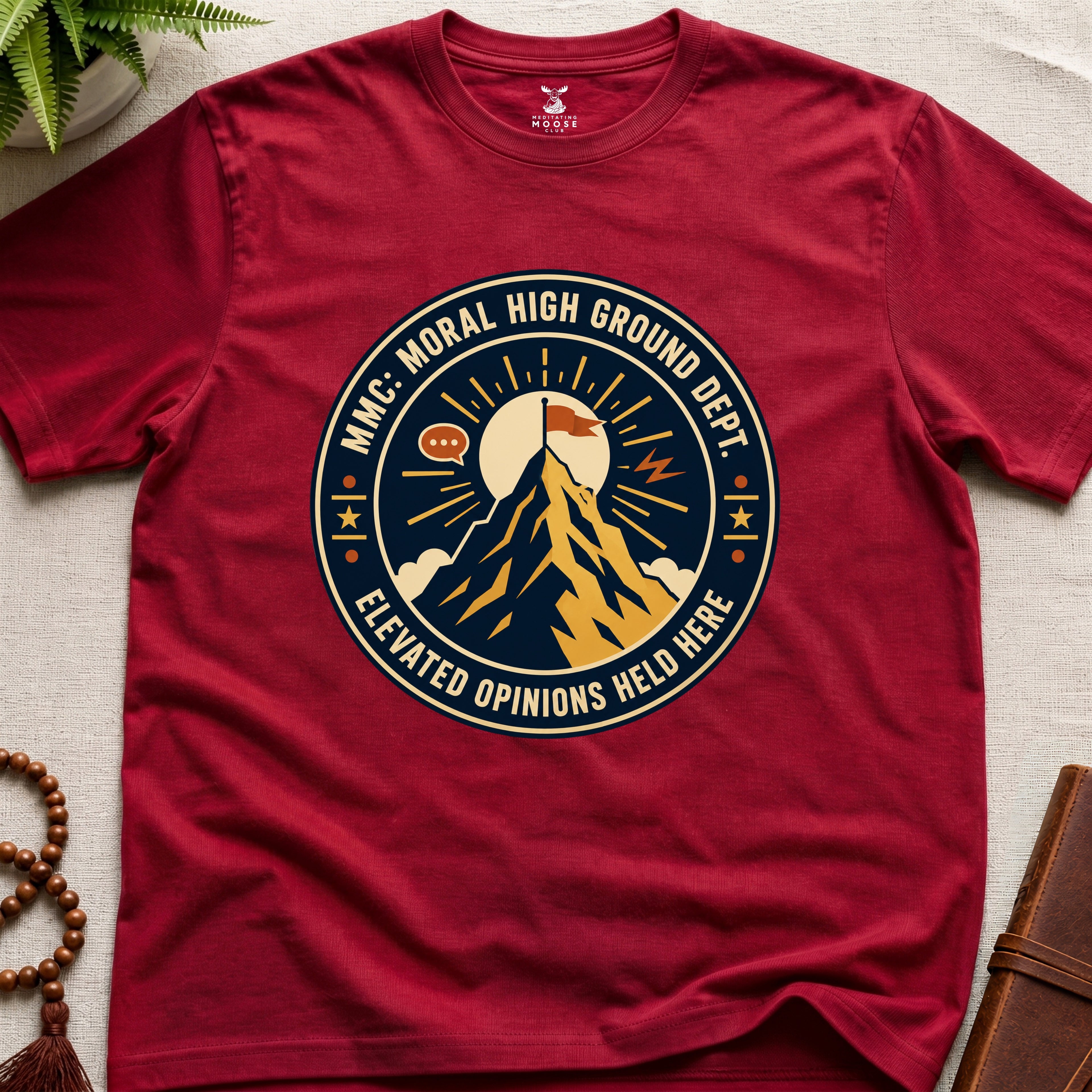 Red t-shirt badge graphic with a mountain and text "moral High Ground Dept." on a light surface.