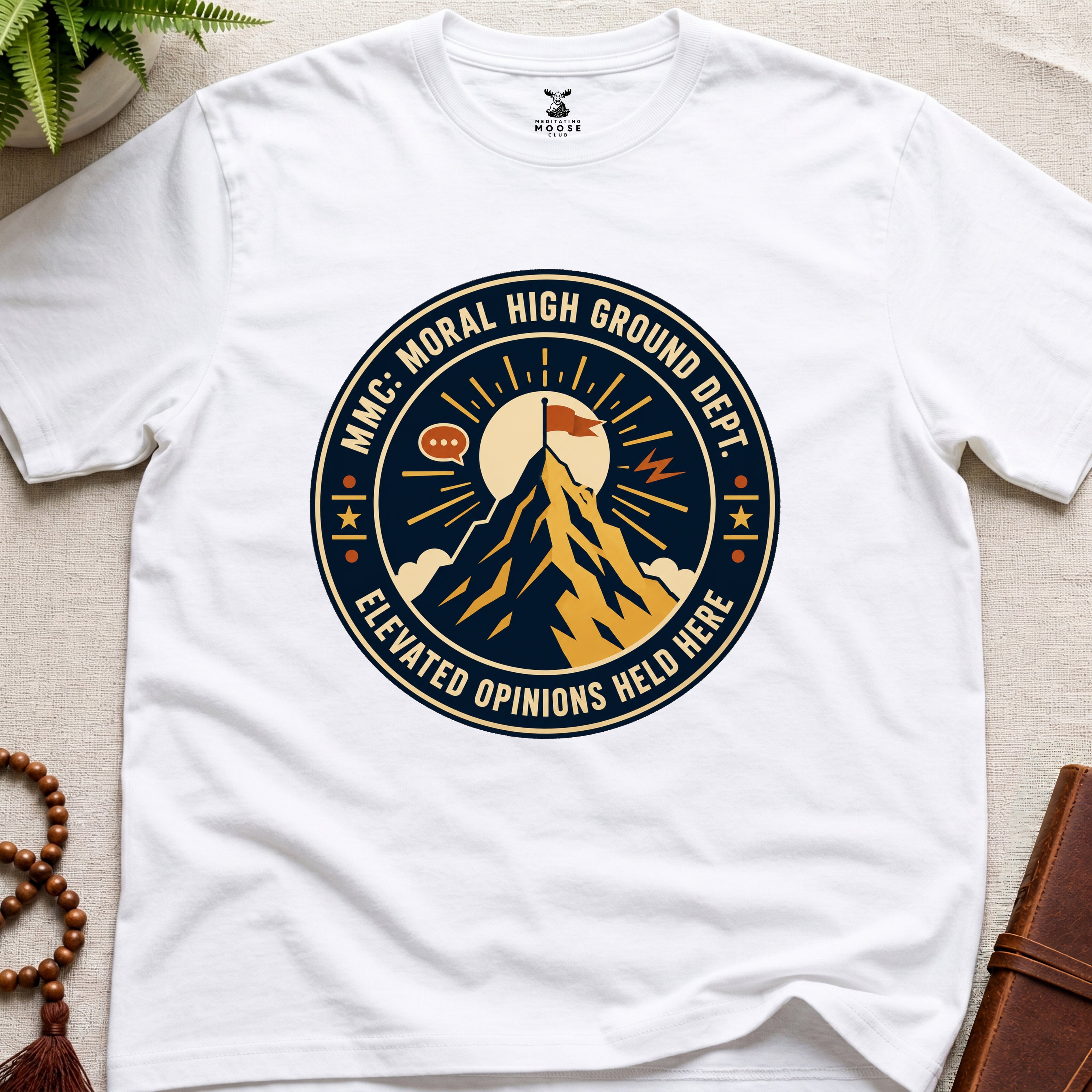 White t-shirt badge graphic with a mountain and text "moral High Ground Dept." on a light surface.