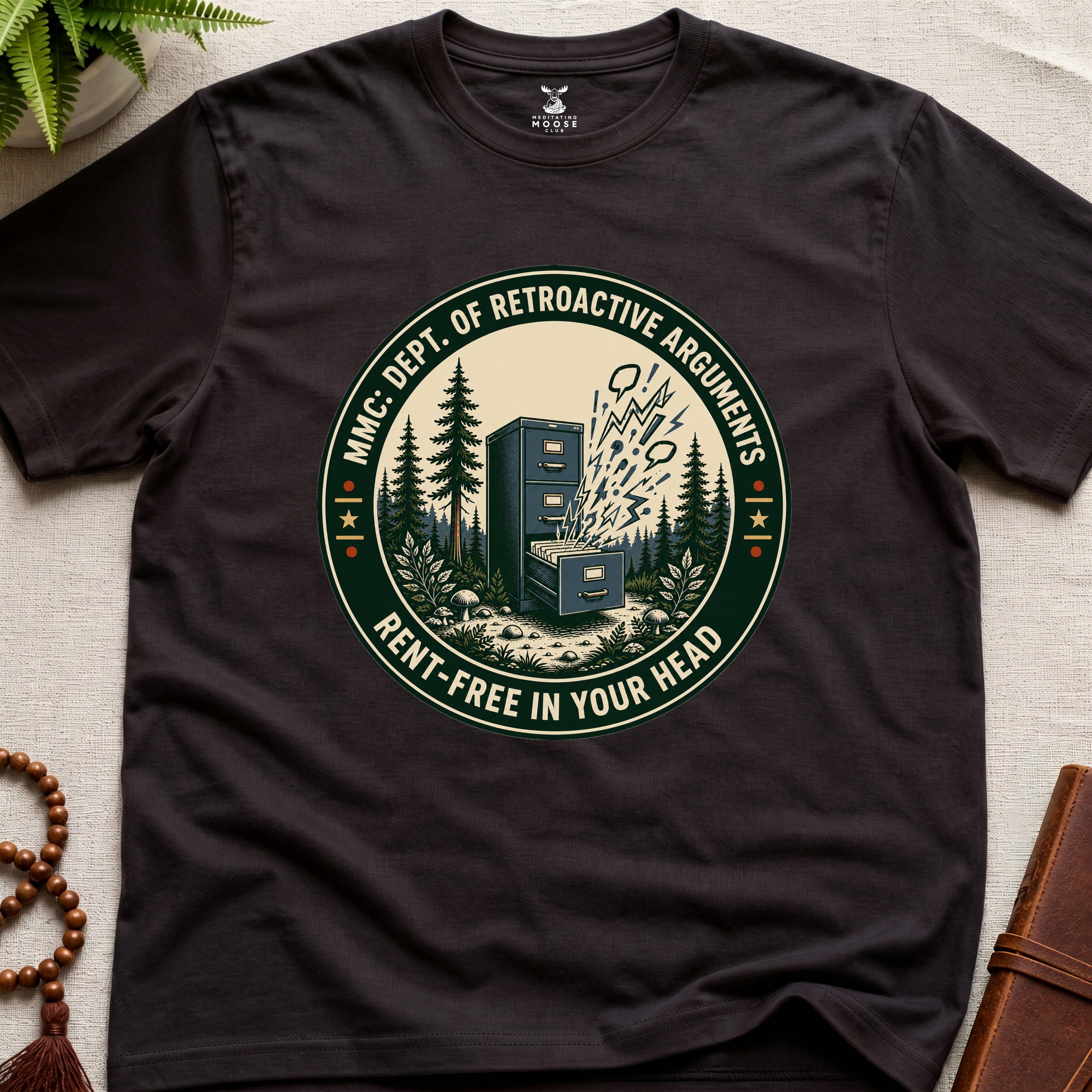 Dark brown t-shirt with a badge graphic design "Dept. of retroactive arguments" on a light surface.
