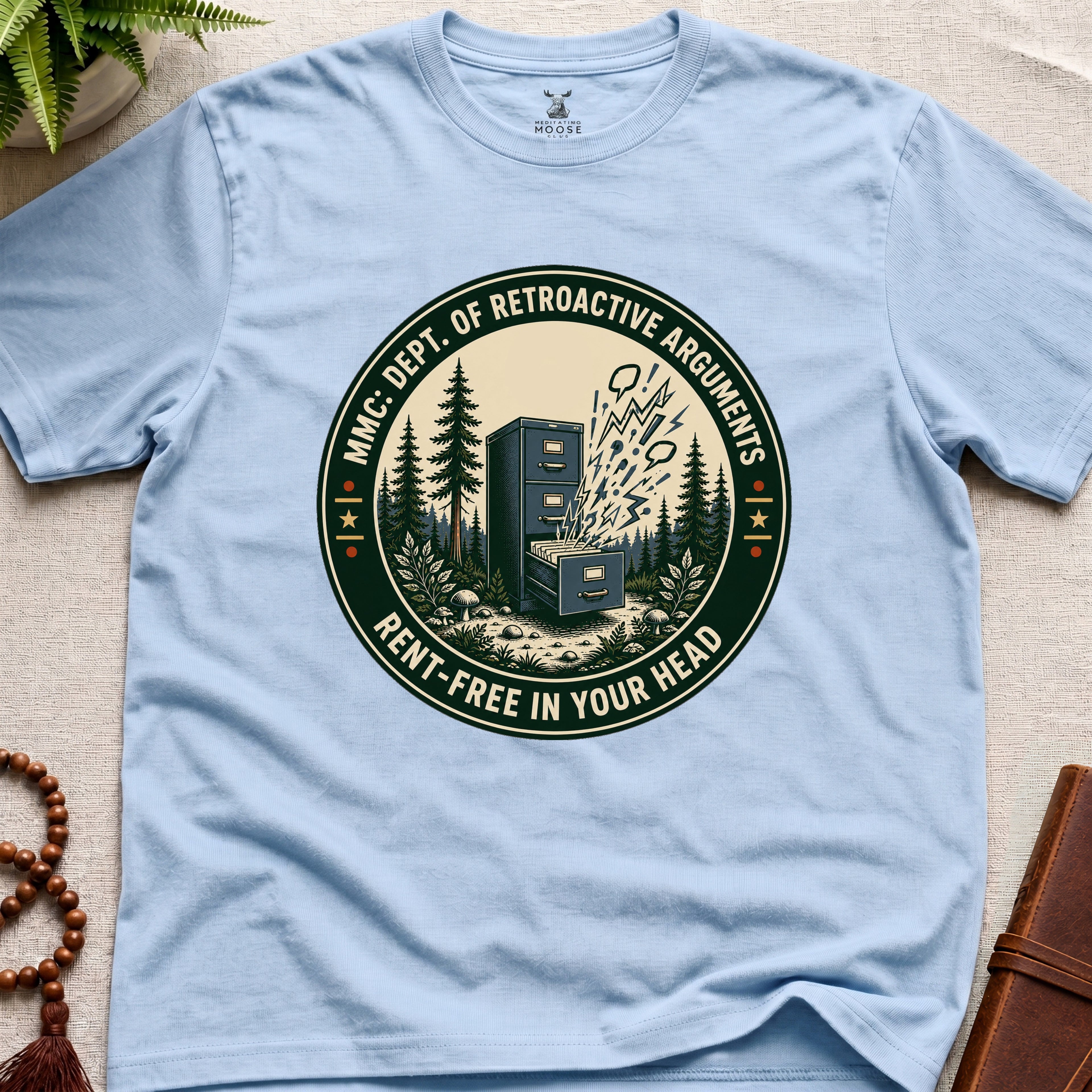 Light blue t-shirt with a badge graphic design "Dept. of retroactive arguments" on a light surface.