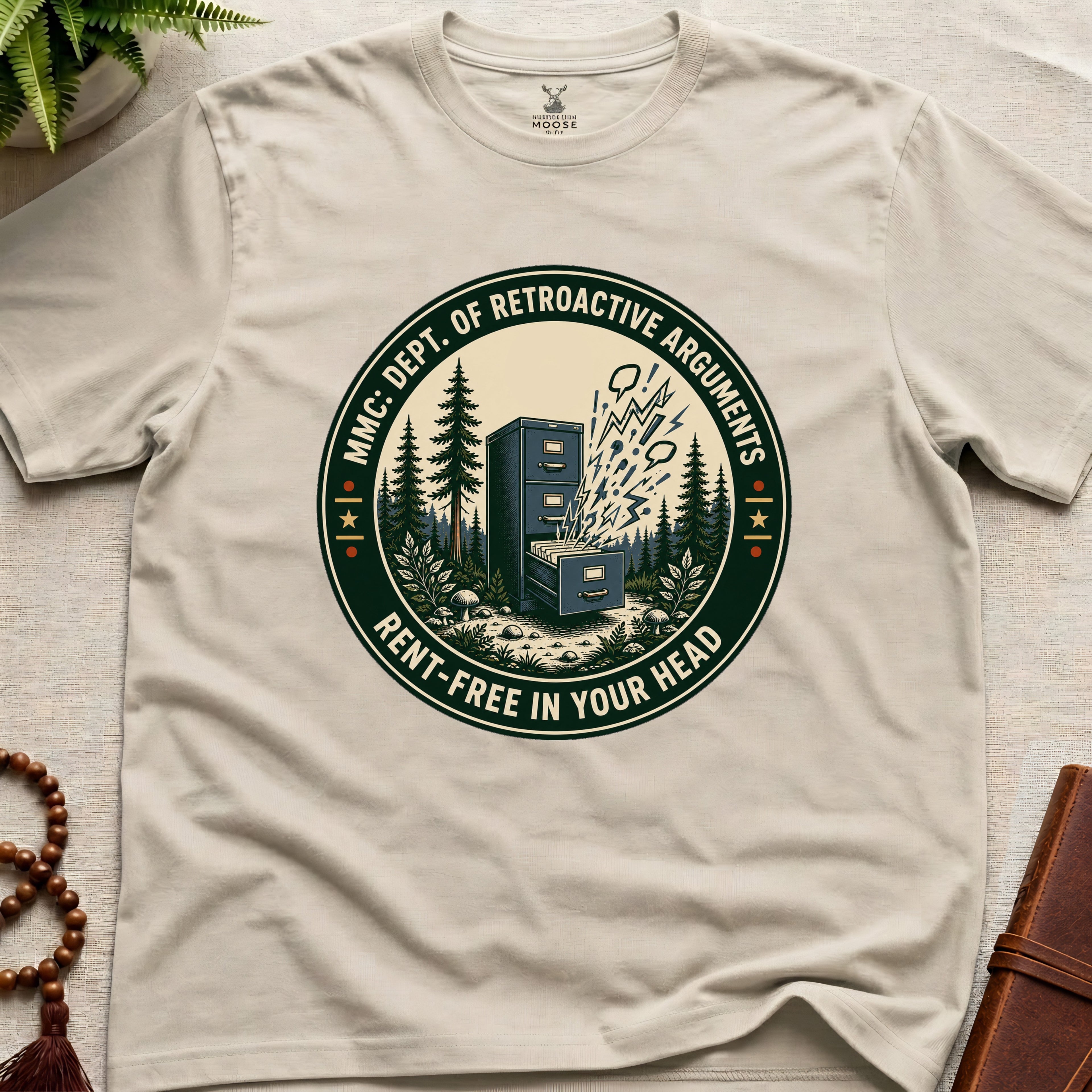 Beige t-shirt with a badge graphic design "Dept. of retroactive arguments" on a light surface.
