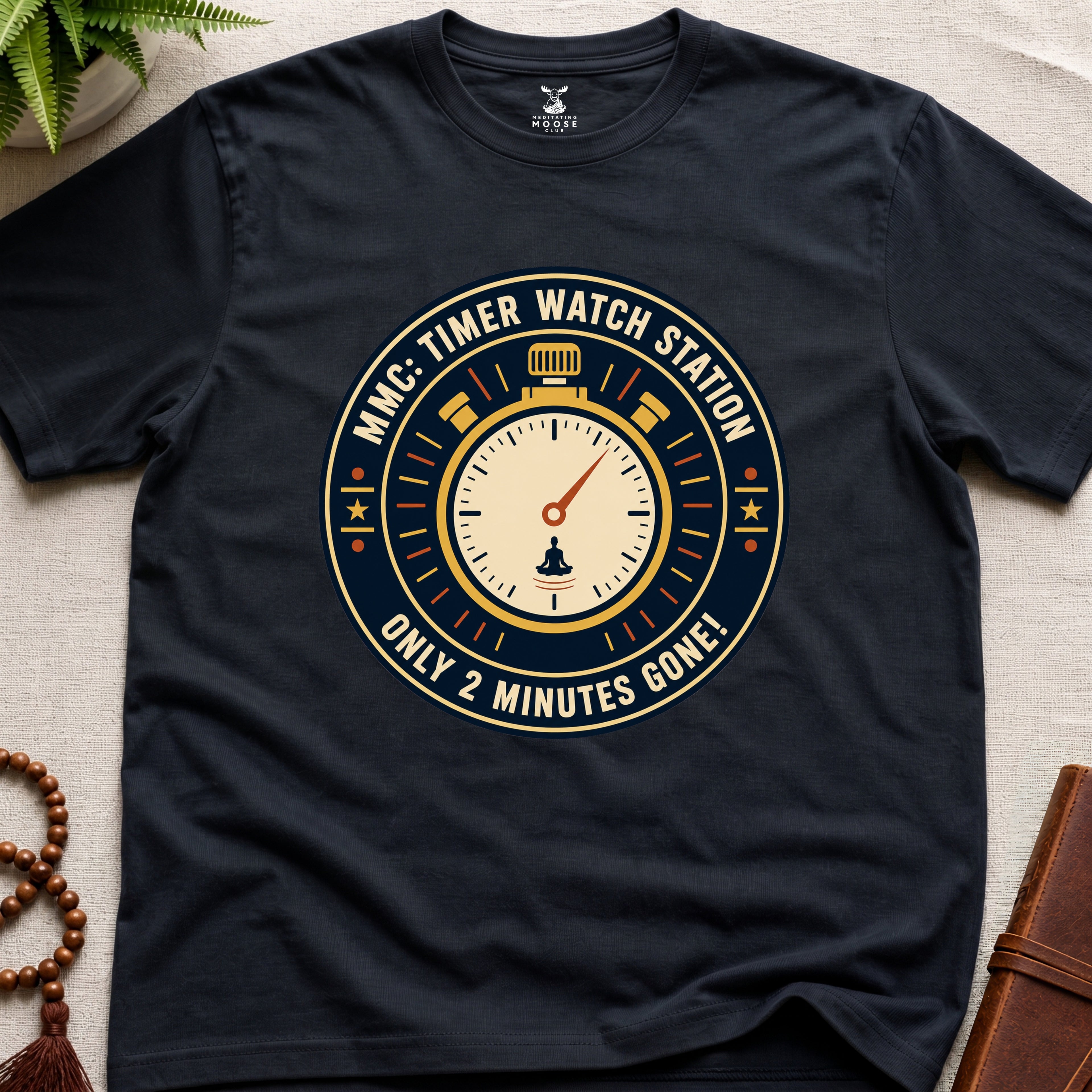 Black t-shirt with a clock graphic and text "only 2 minutes gone!" on a beige surface.