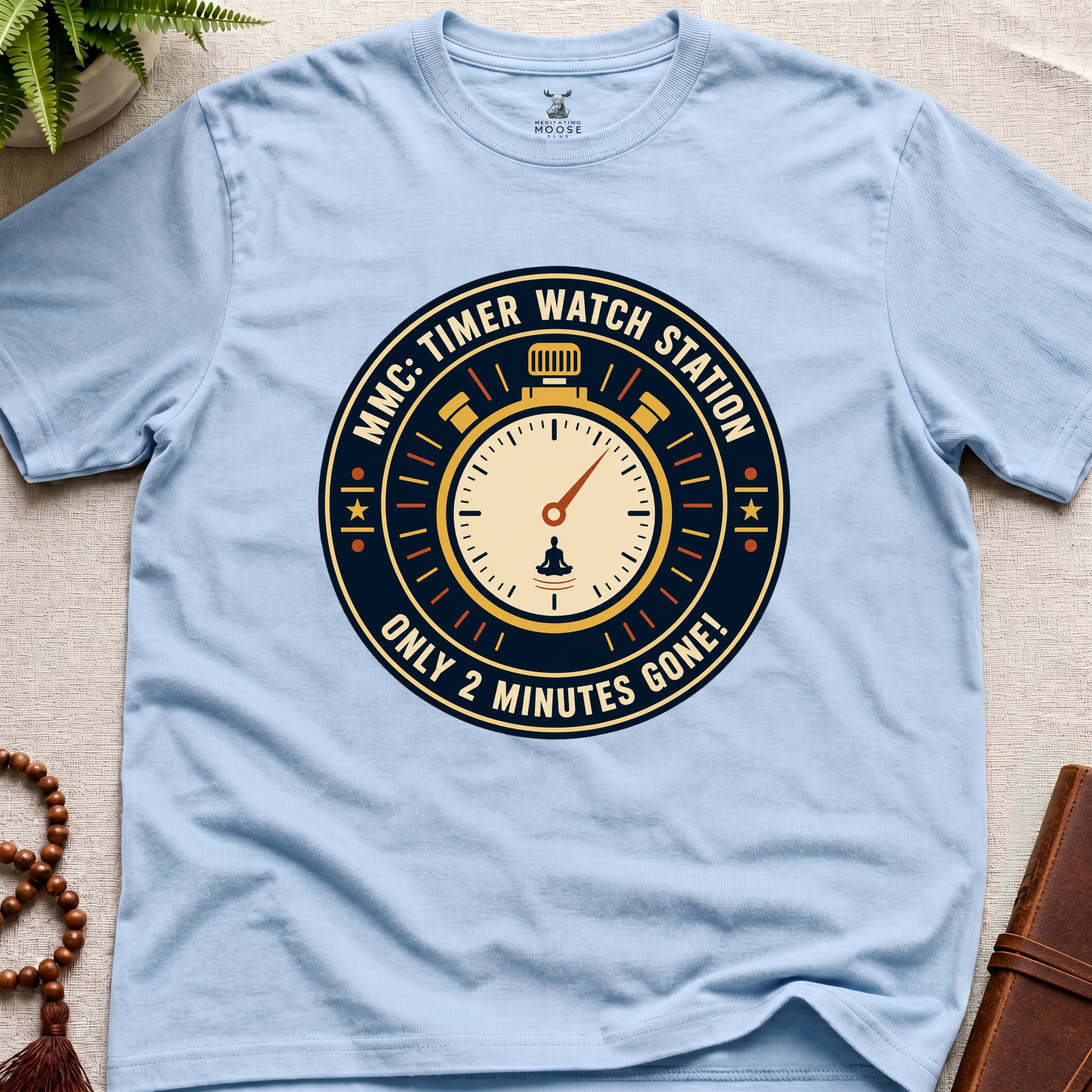 Light blue t-shirt with a clock graphic and text "only 2 minutes gone!" on a beige surface.