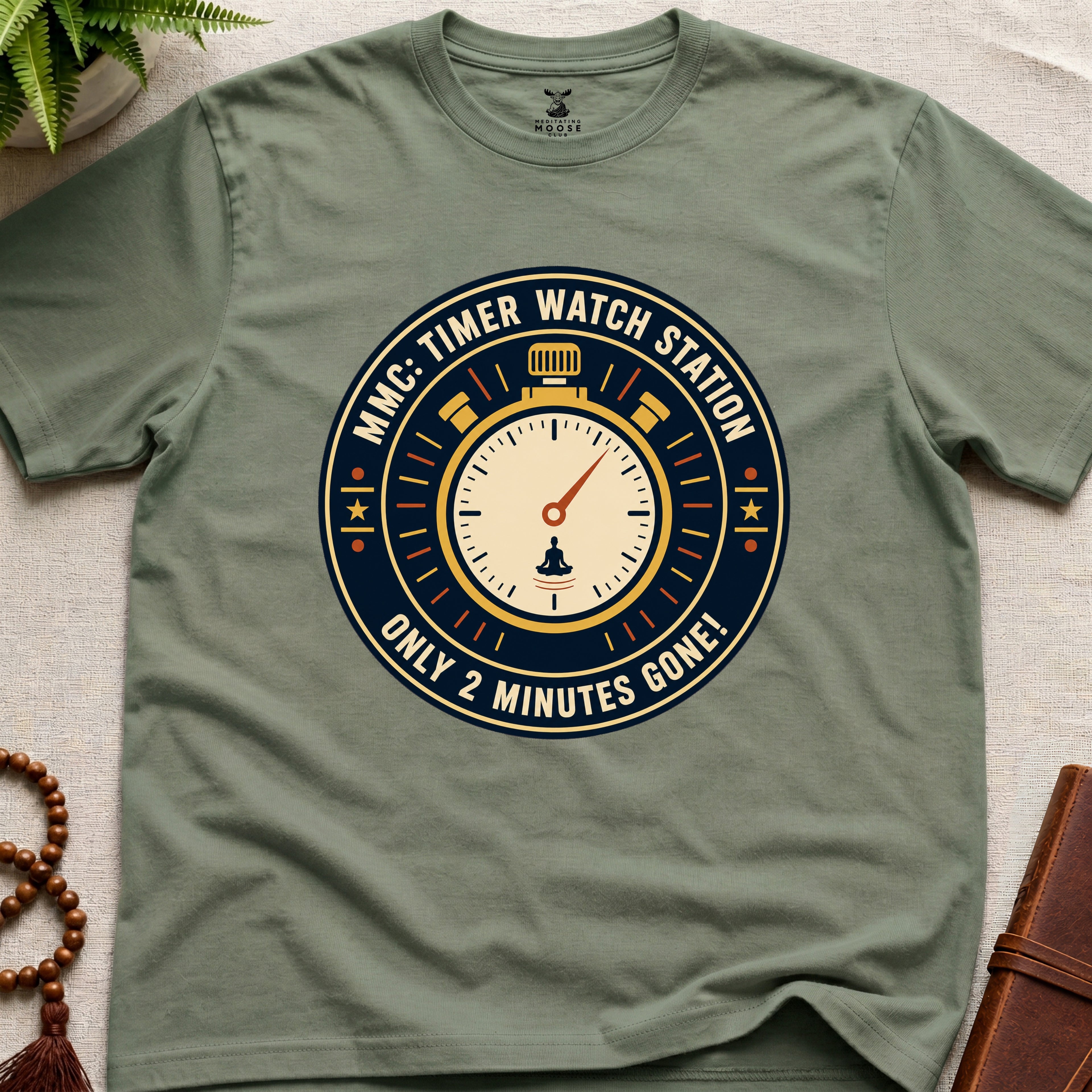 Military Green t-shirt with a clock graphic and text "only 2 minutes gone!" on a beige surface.