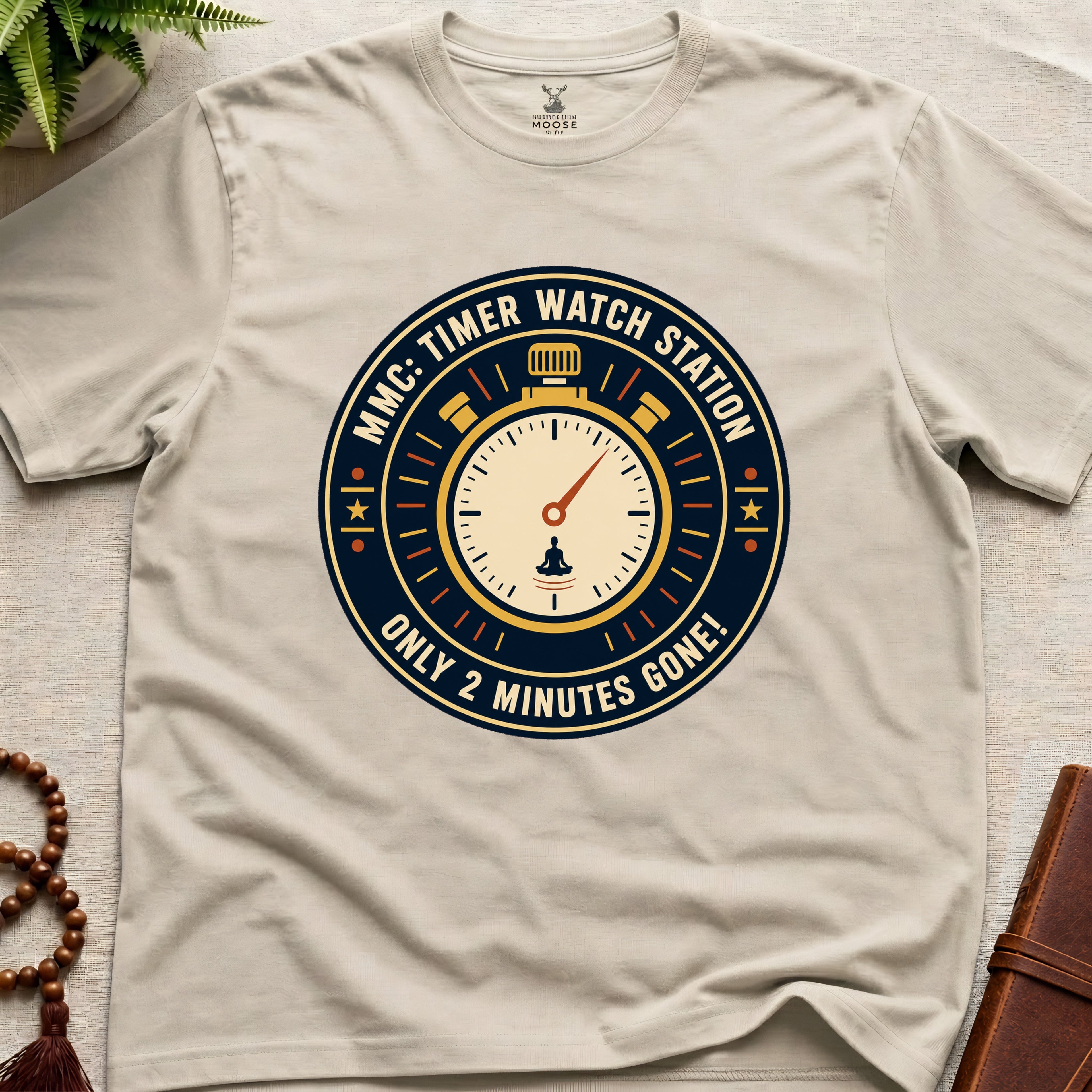 Beige t-shirt with a clock graphic and text "only 2 minutes gone!" on a beige surface.