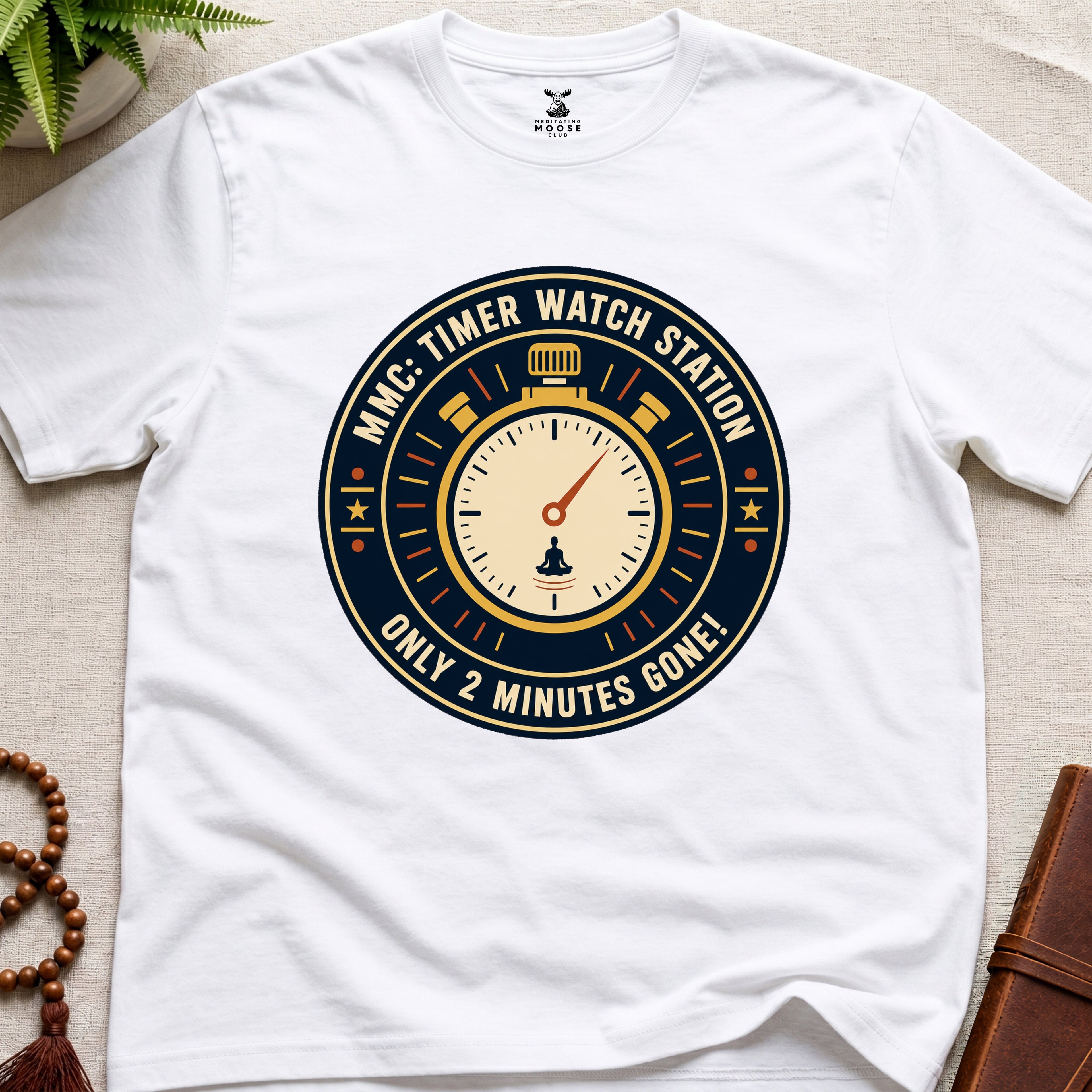 White t-shirt with a clock graphic and text "only 2 minutes gone!" on a beige surface.