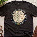 Dark Brown t-shirt with a circular badge design featuring text "established in chaos" and sacred geometry graphics on a light wooden surface.
