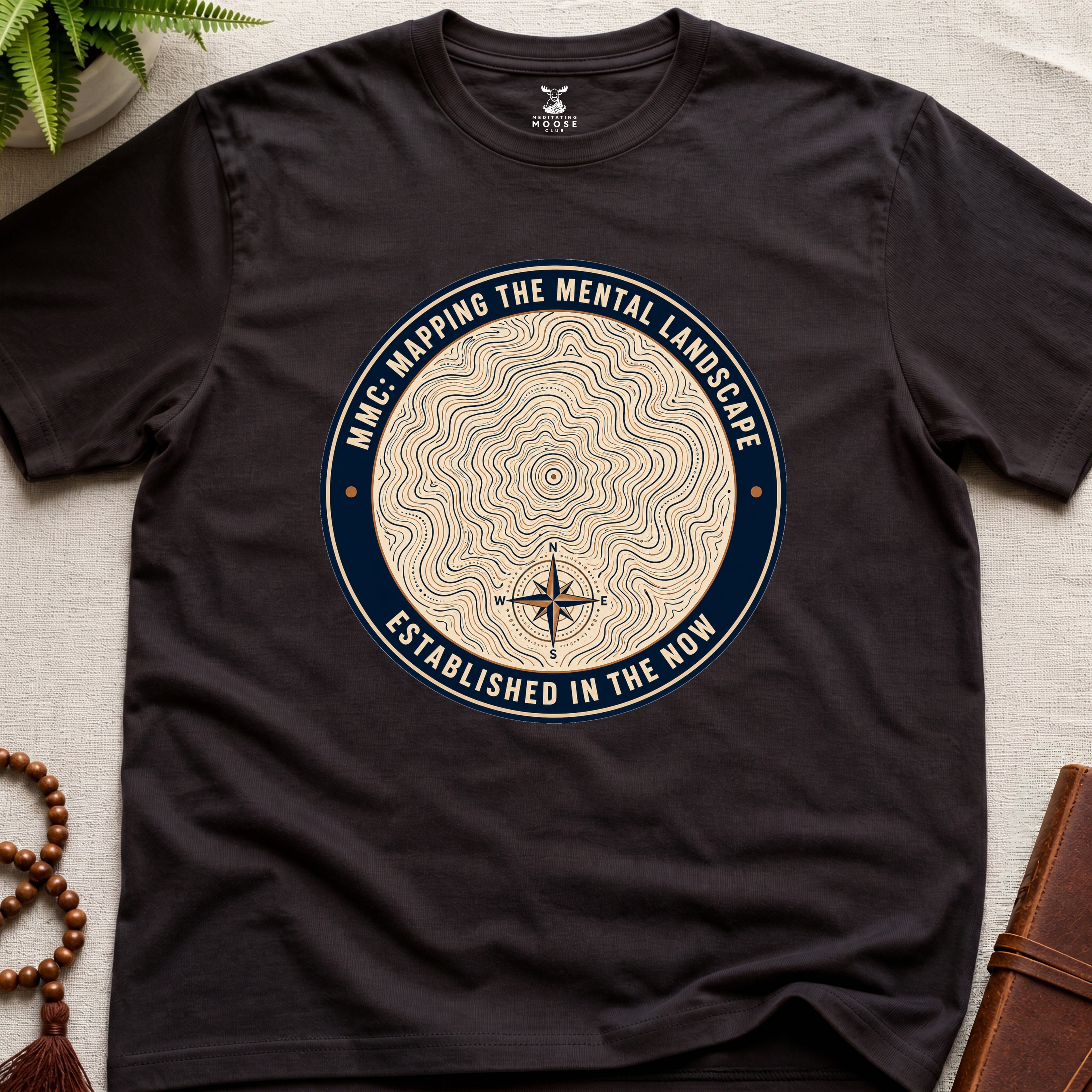 Dark brown mindfulness t-shirt with topographic landscape badge design featuring compass