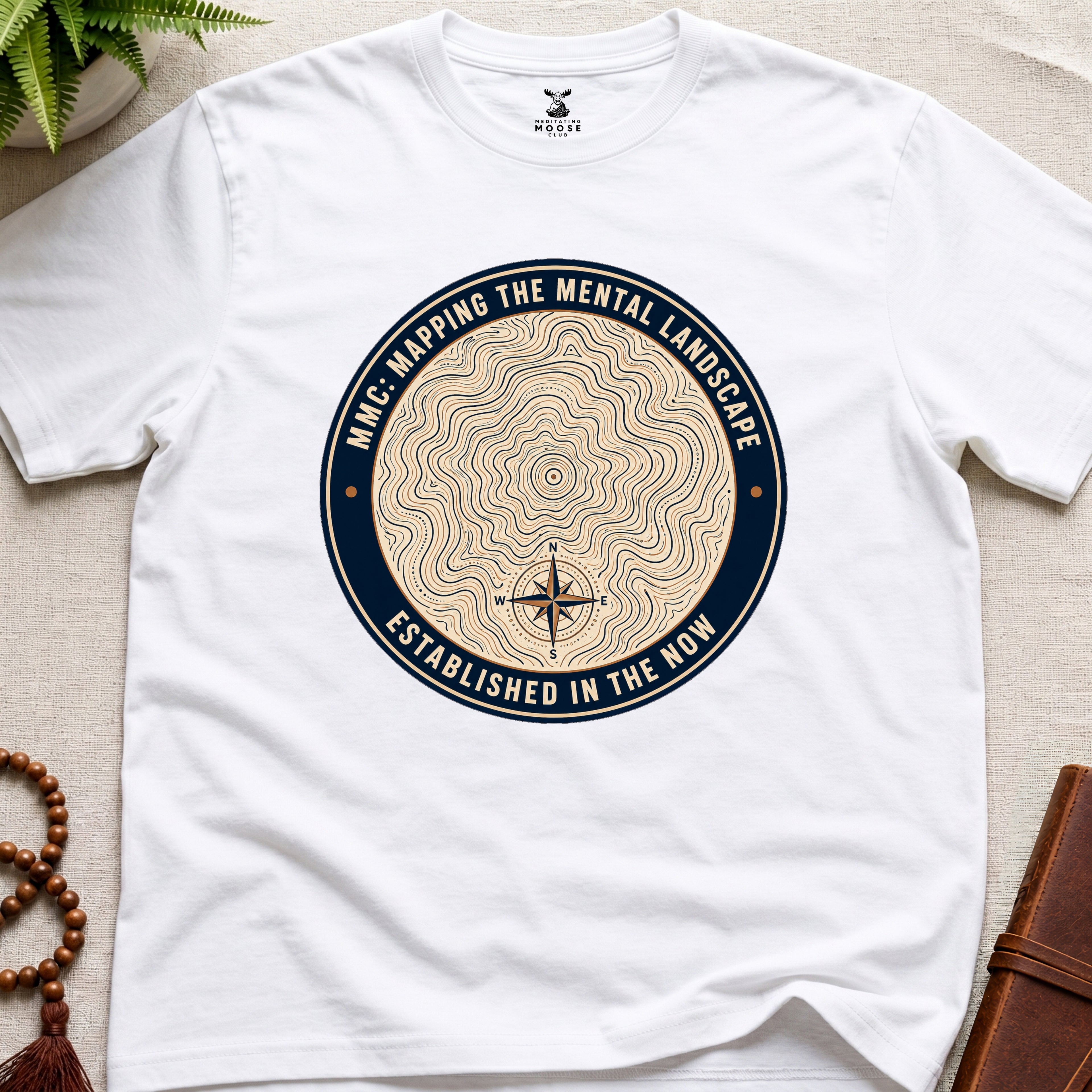 White mindfulness t-shirt with topographic landscape badge design featuring compass