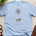 Light blue t-shirt with botanical design and text on a beige surface.