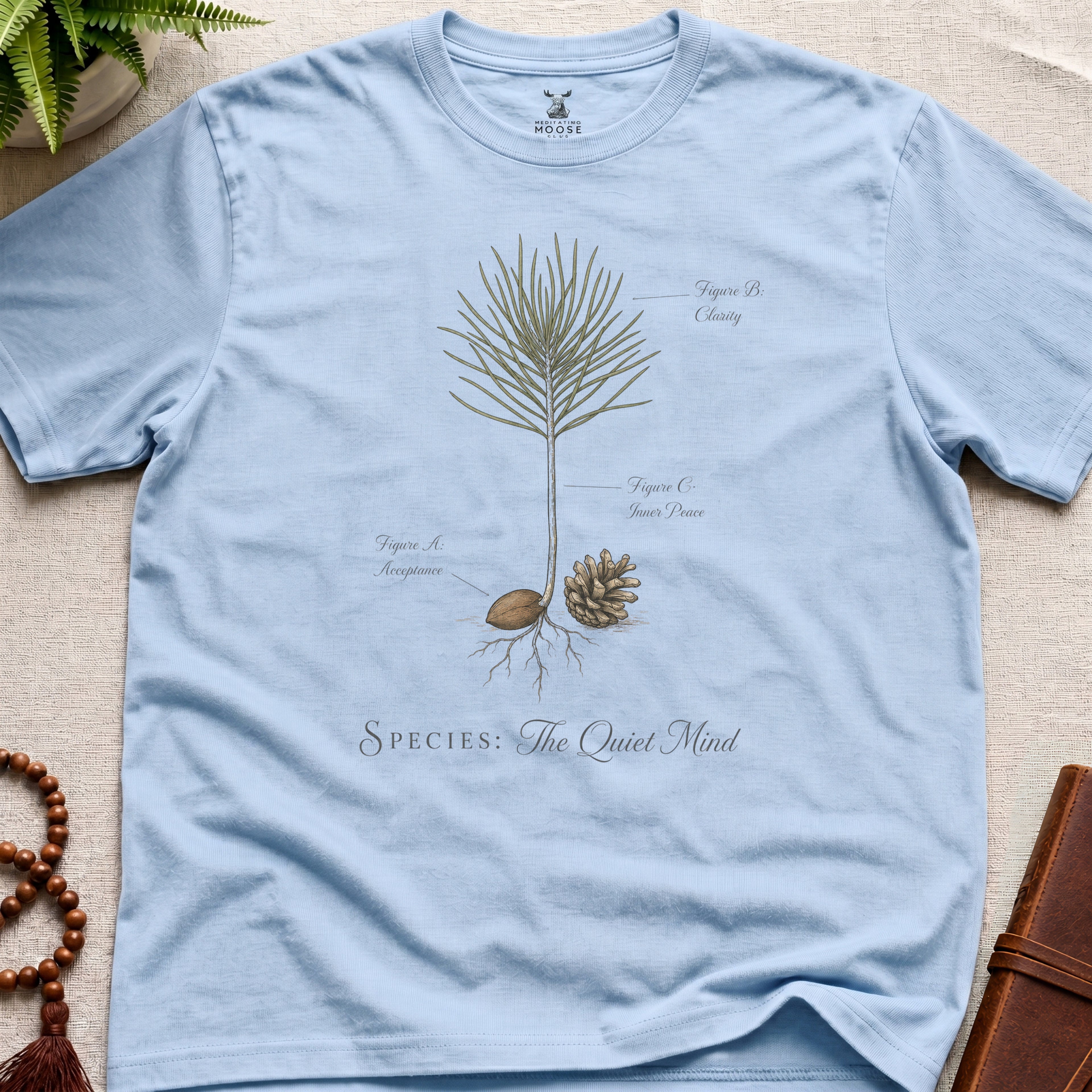 Light blue t-shirt with botanical design and text on a beige surface.