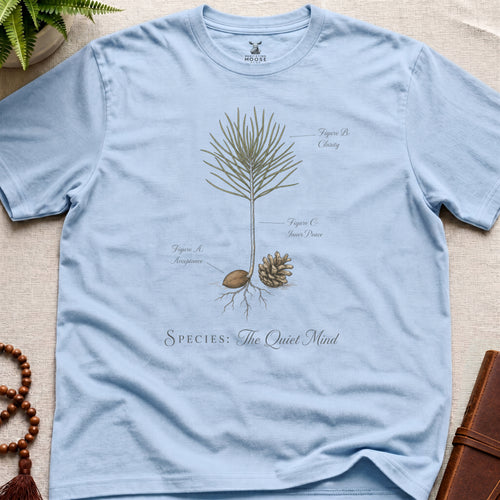 Light blue t-shirt with botanical design and text on a beige surface.