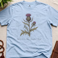 Light blue t-shirt with botanical thistle design and text on a beige surface.