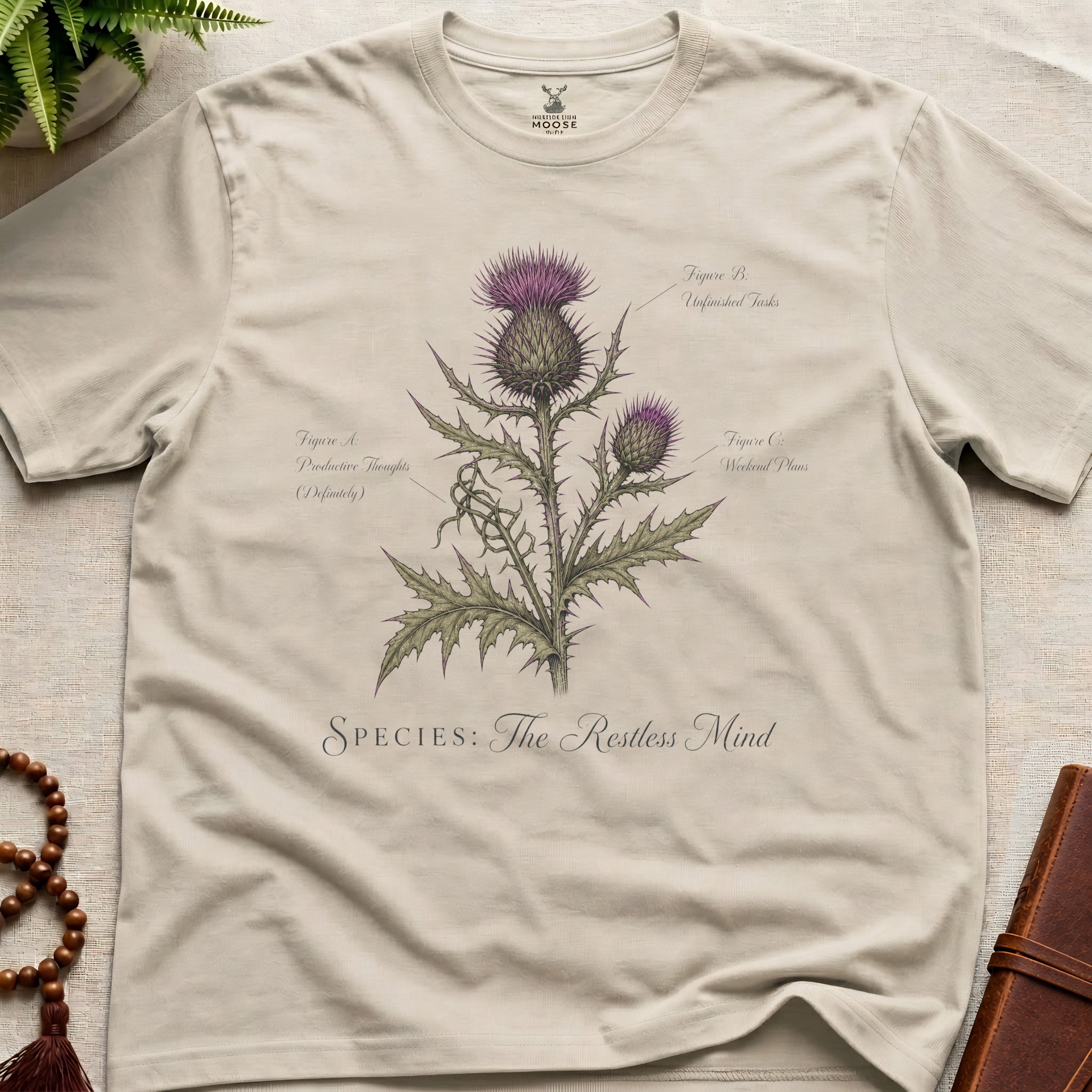 Beige t-shirt with botanical design and text on a light wooden surface.