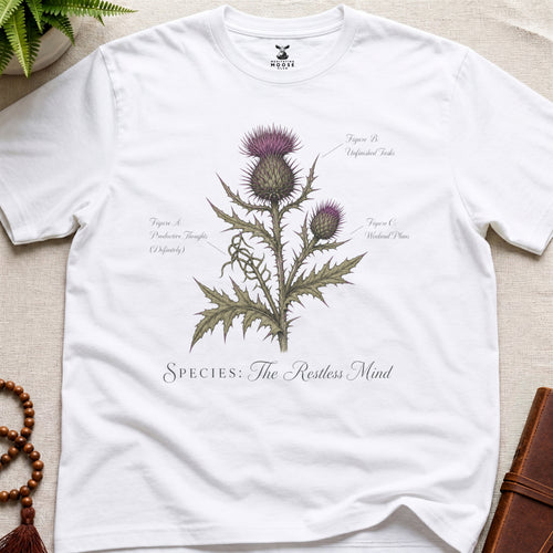 White t-shirt with a thistle plant design and text on a beige surface.