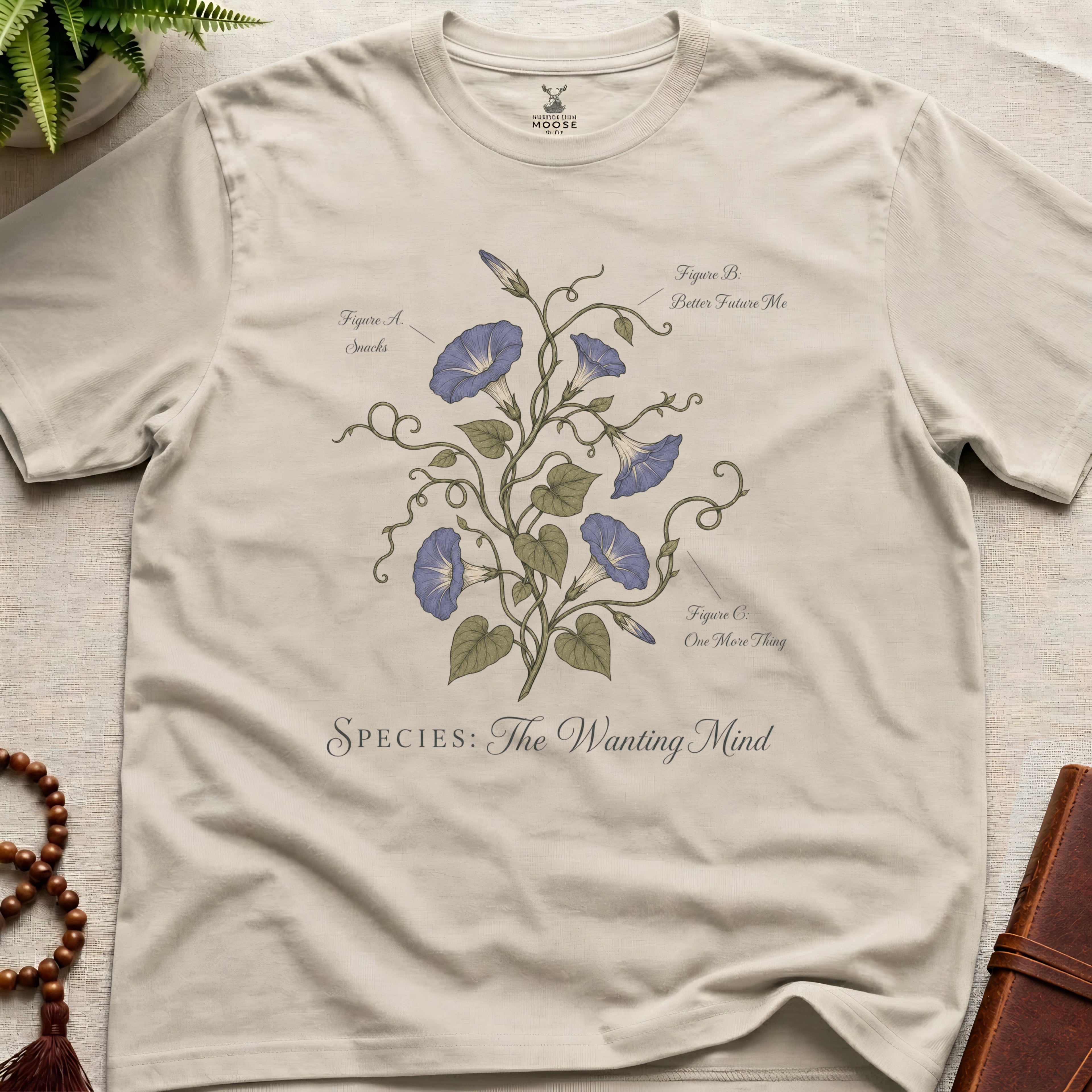 Beige t-shirt with botanical design and text on a light surface.