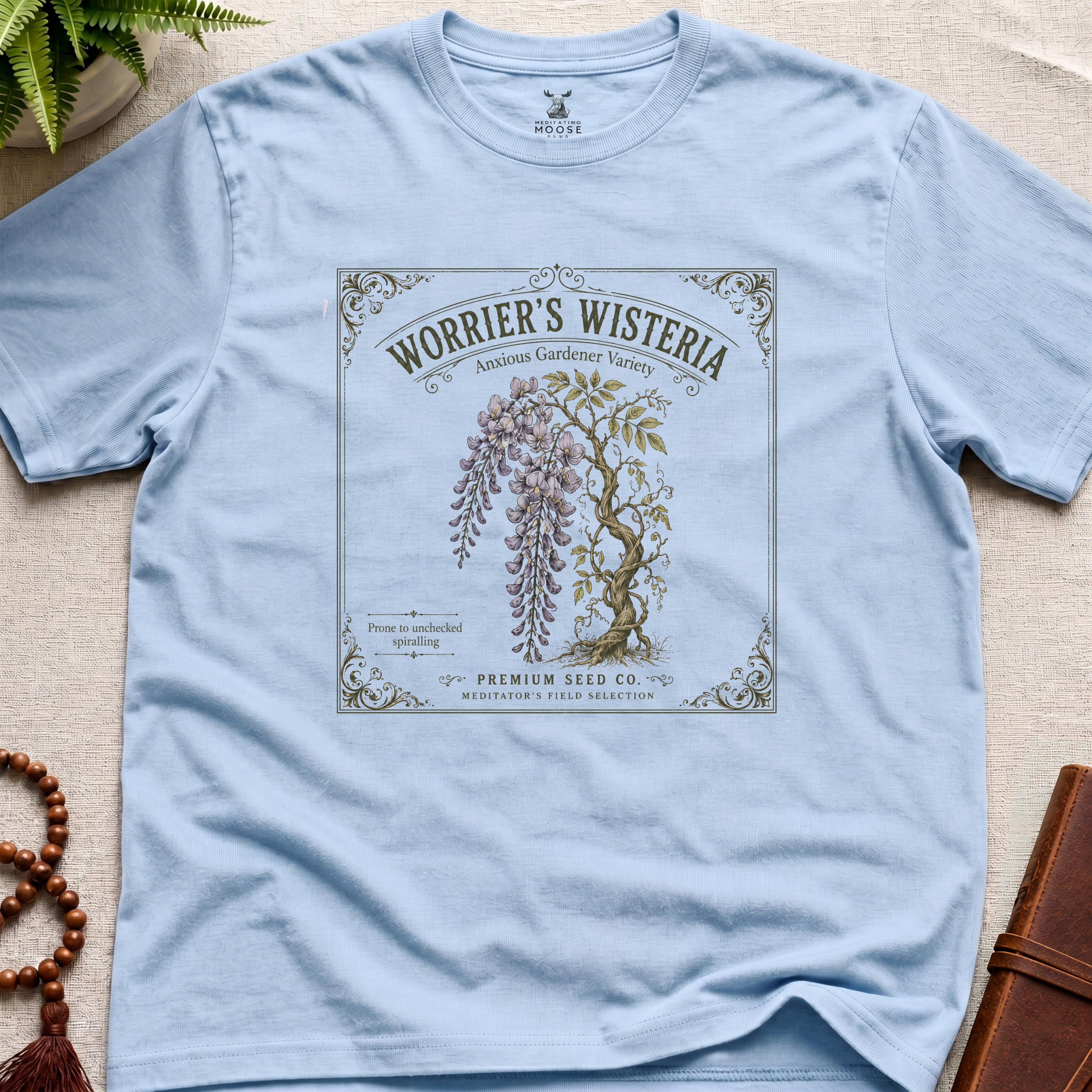 Light blue t-shirt with a vintage-style seed packet design featuring wisteria on a beige surface.