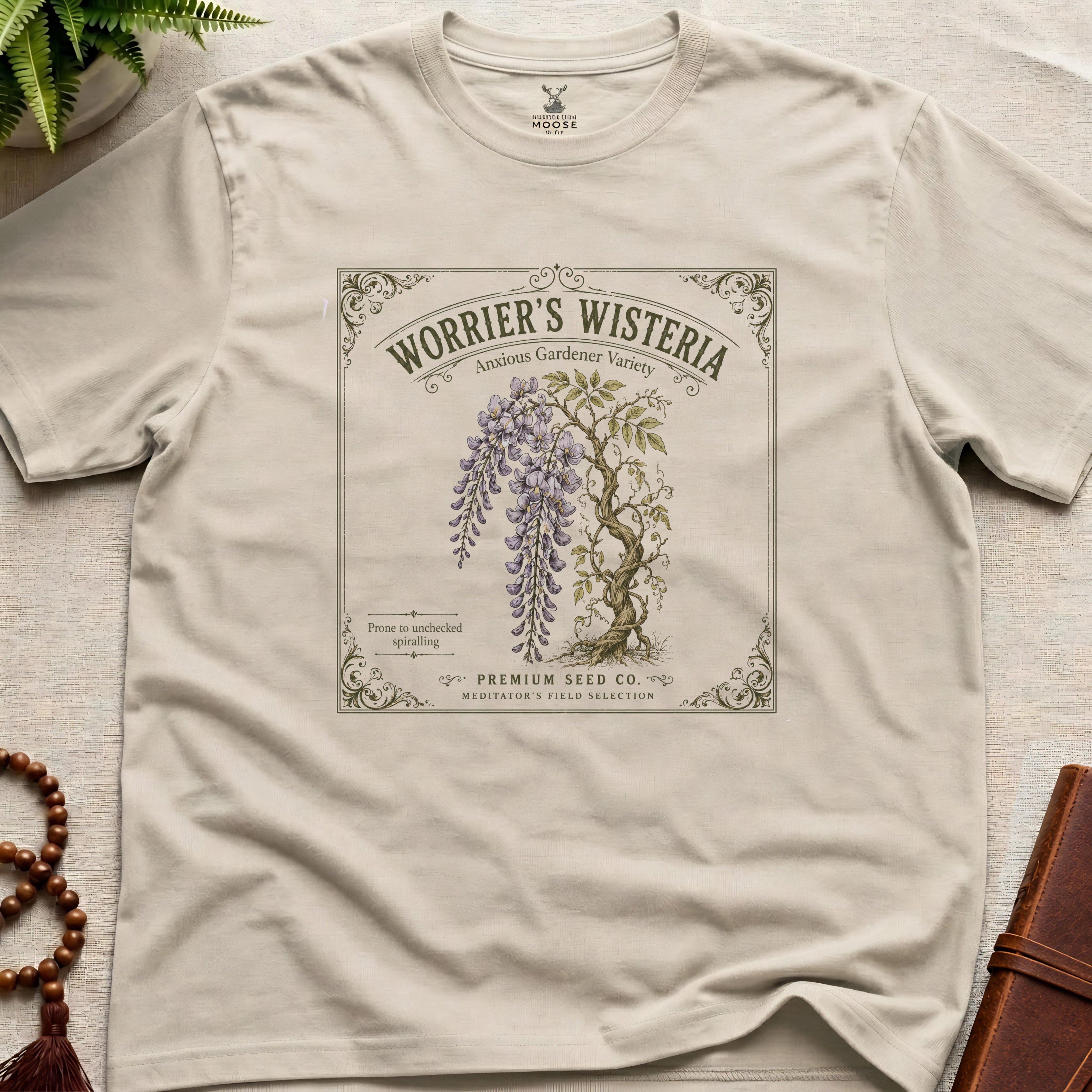 Beige t-shirt with a Wisteria seed packet design on a light surface.