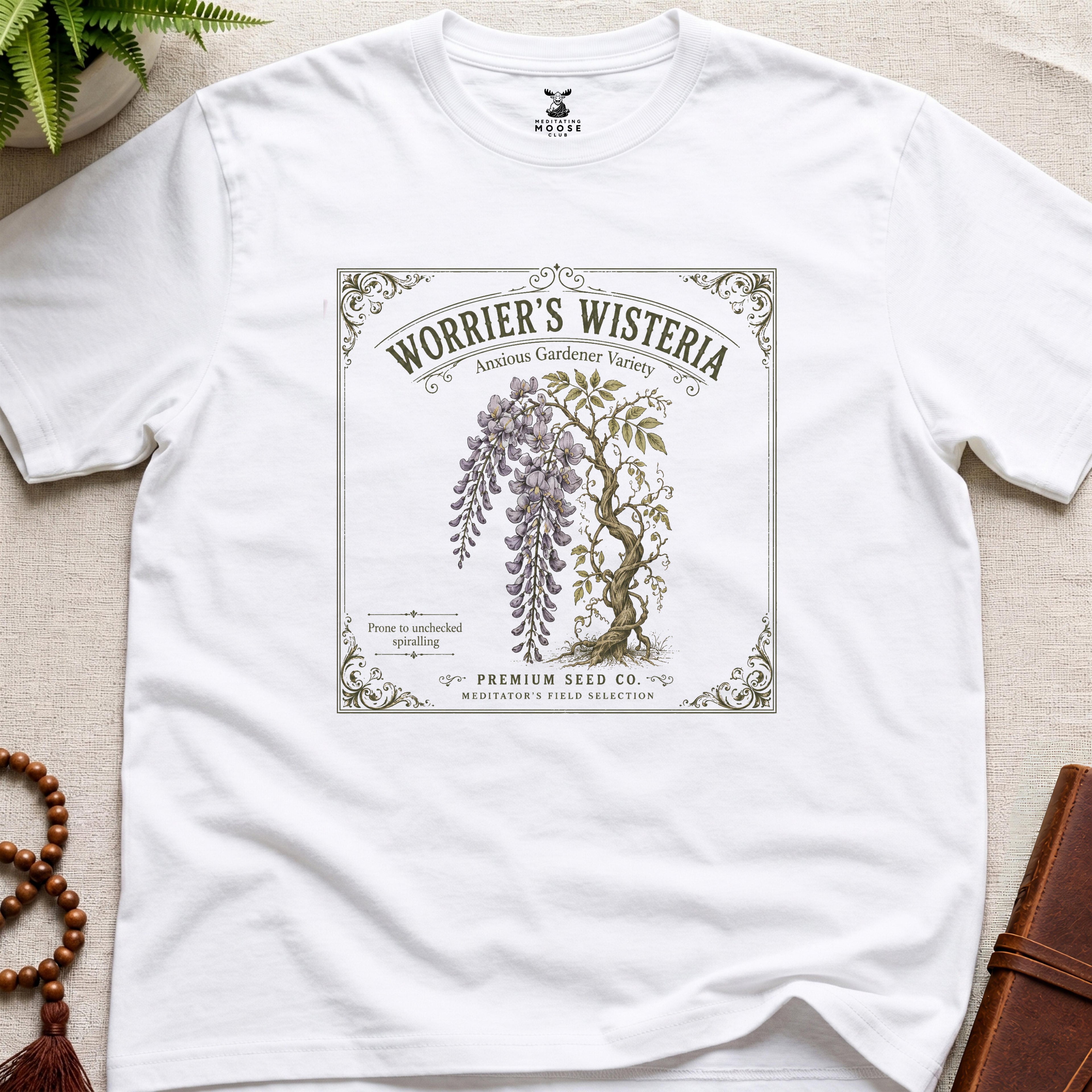 White t-shirt with 'Worrier's Wisteria' seed packet design on a beige surface.